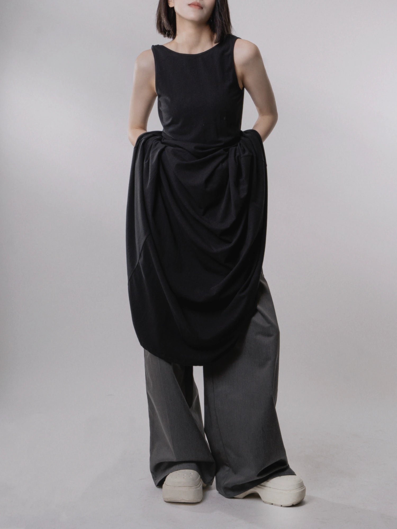 Black backless dress layered over trousers, experimental styling, soft drape and fluid silhouette.