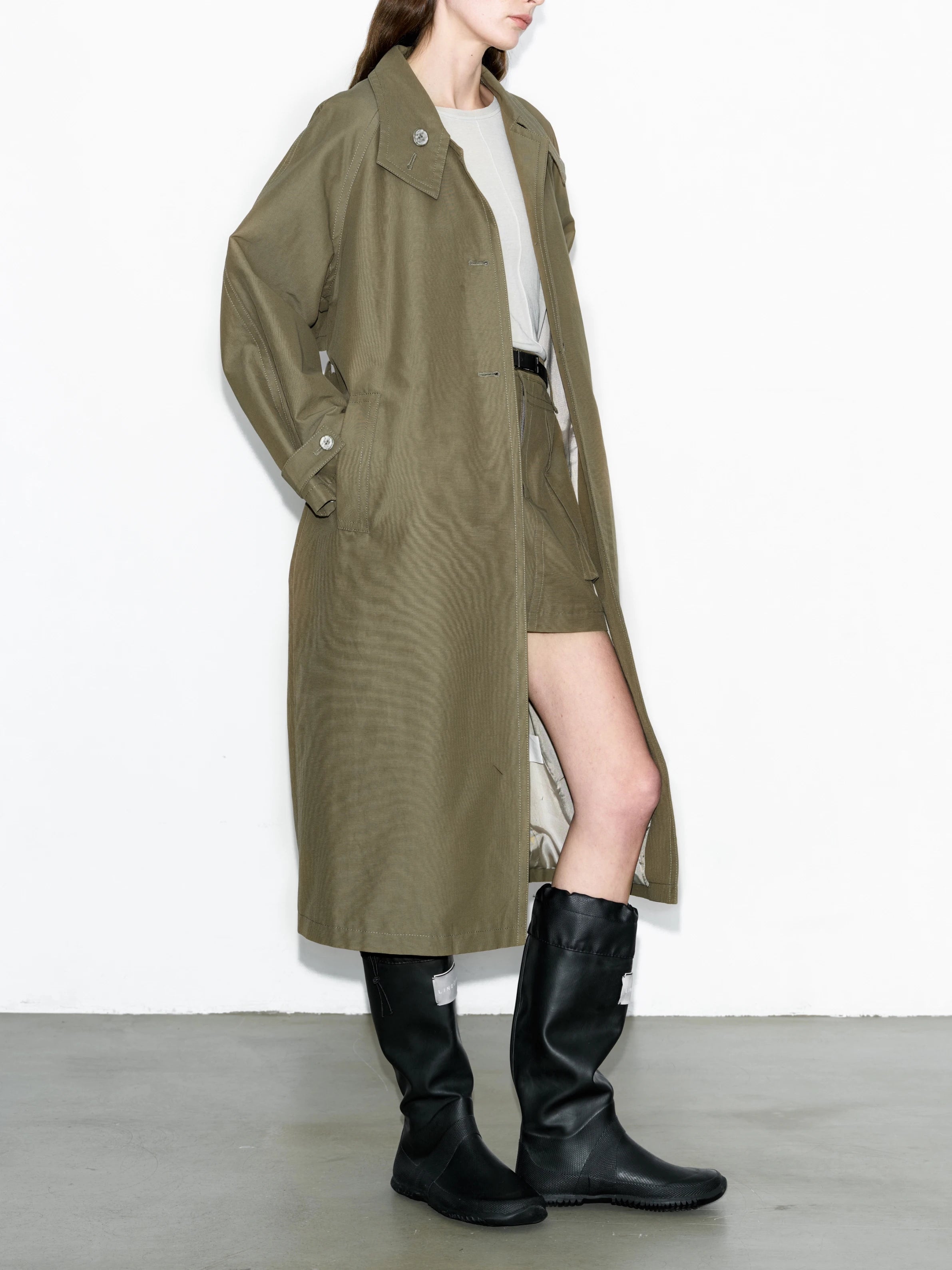 Side angle of army green trench coat, layered back detail visible, long coat paired with knee boots