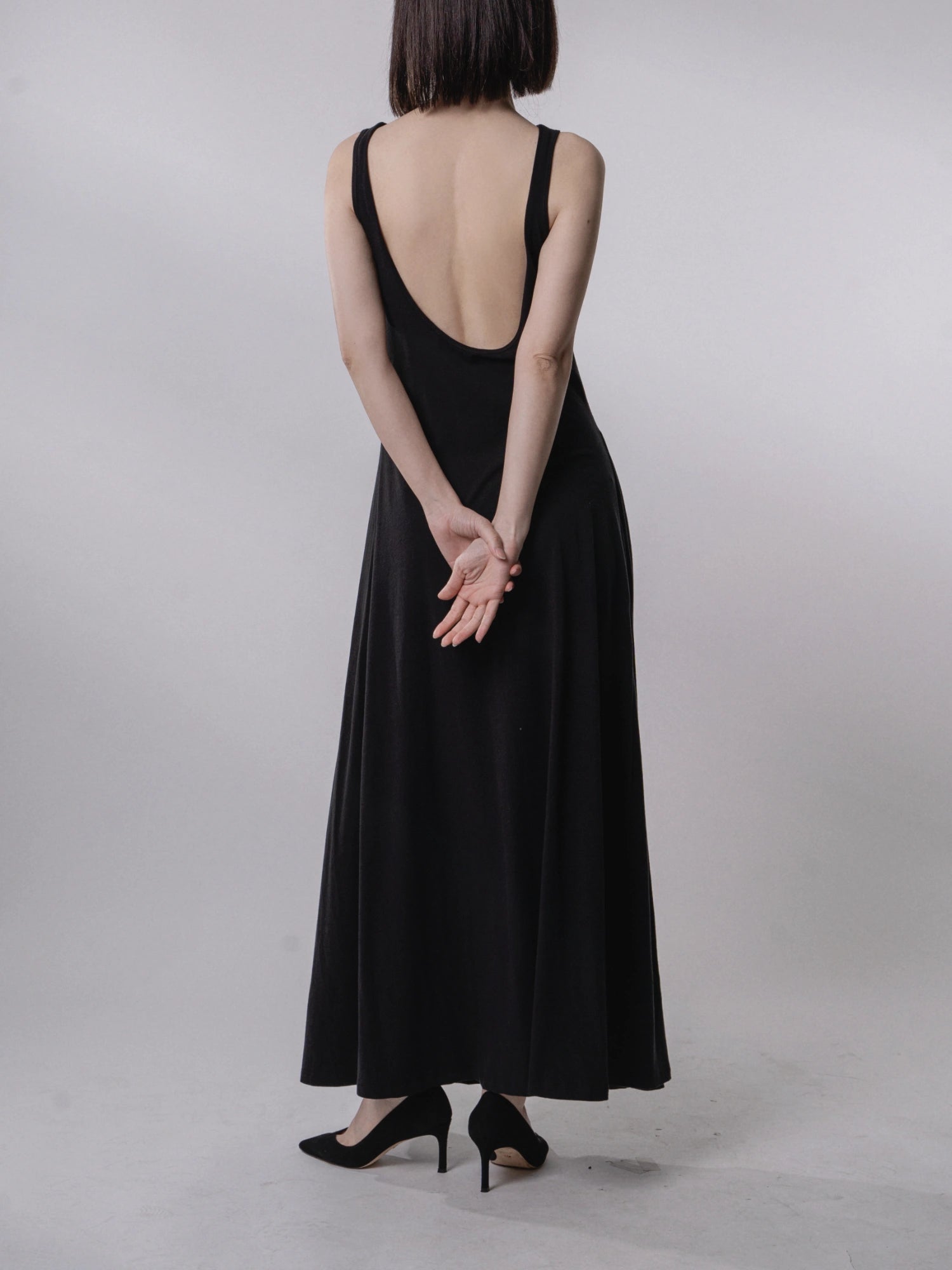 Backless dress rear view, deep U-shaped open back, clean lines, sleeveless, refined drape, elegant posture.