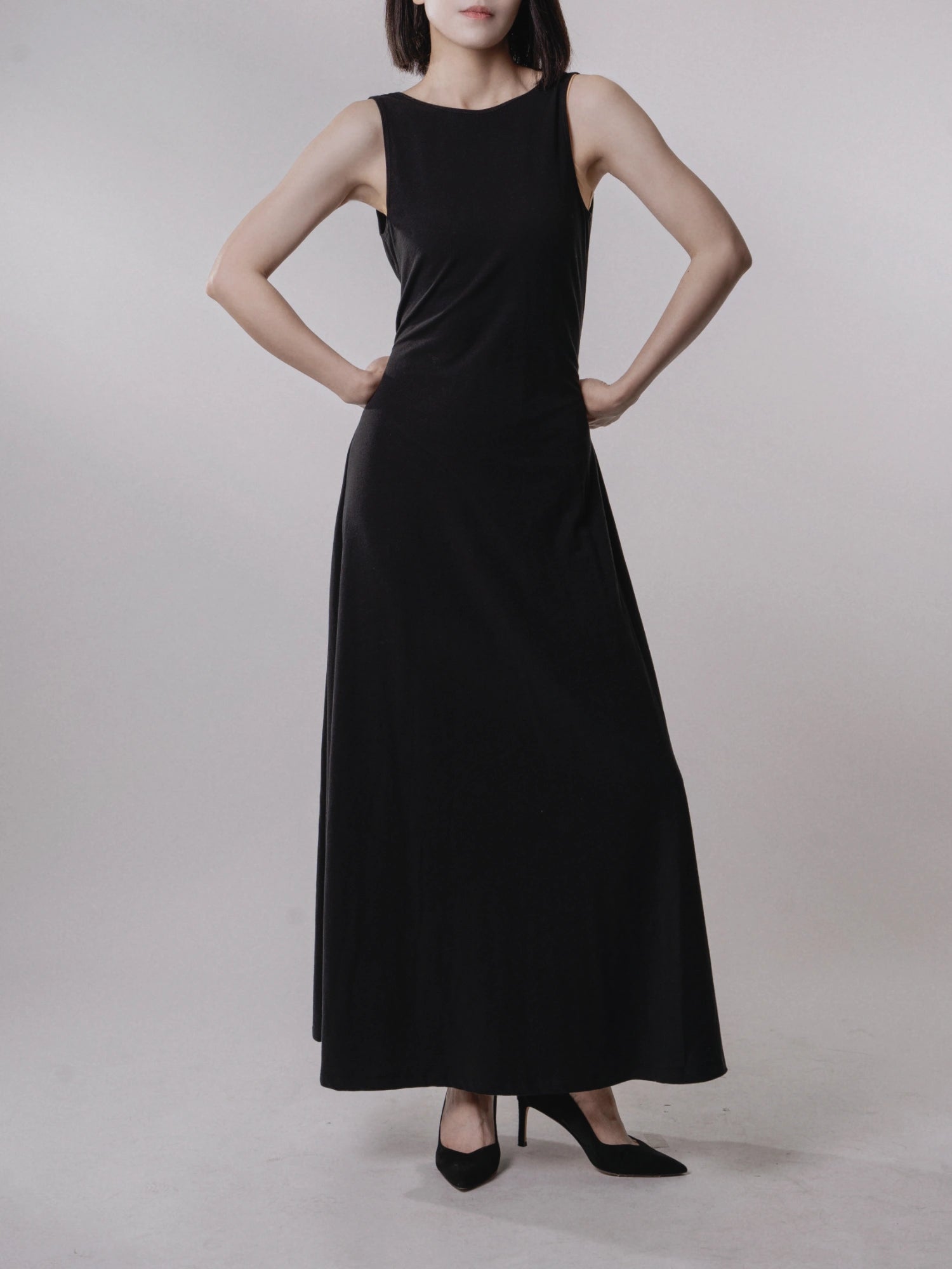 Model in black backless dress hands-on-hip pose, evening wear, refined silhouette.