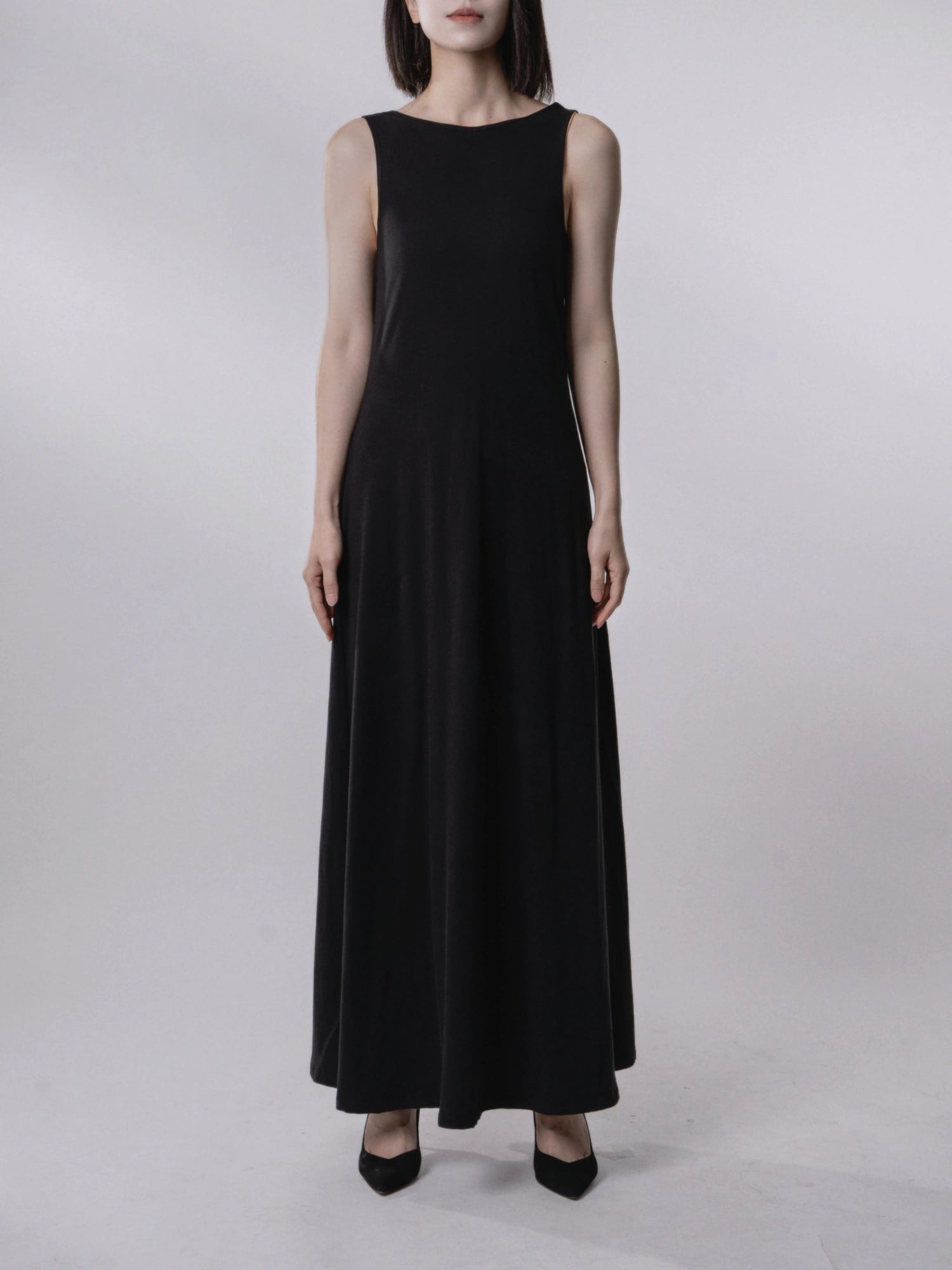 Front view sleeveless black backless dress, clean neckline, long flowing drape, minimalist styling.