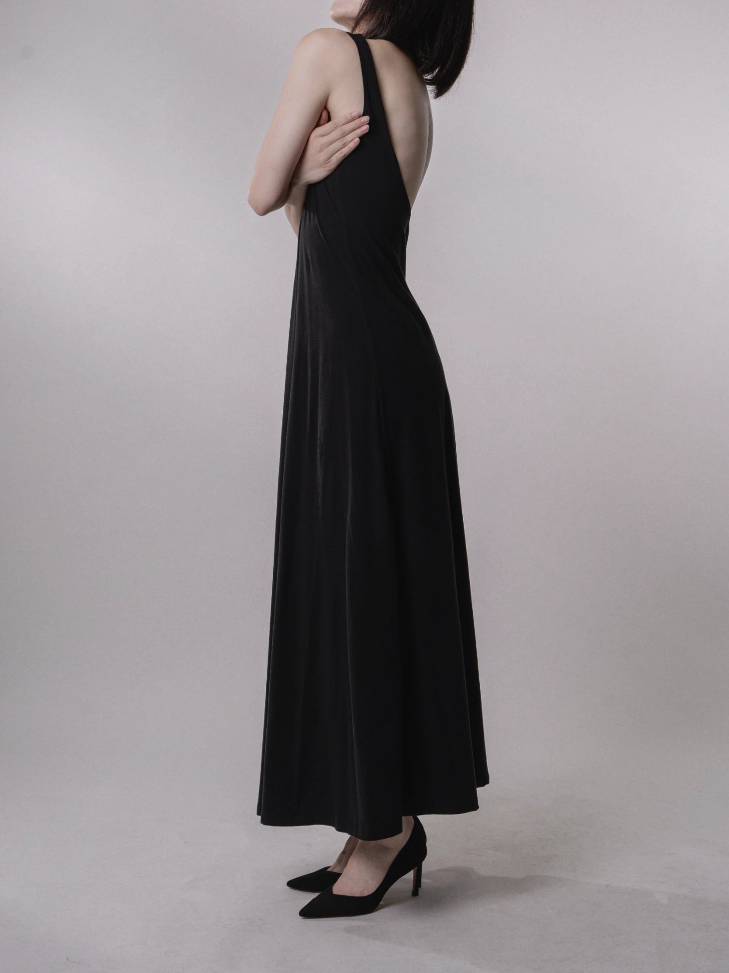 Backless dress side profile, long A-line hem, minimal evening style, structured yet fluid movement.