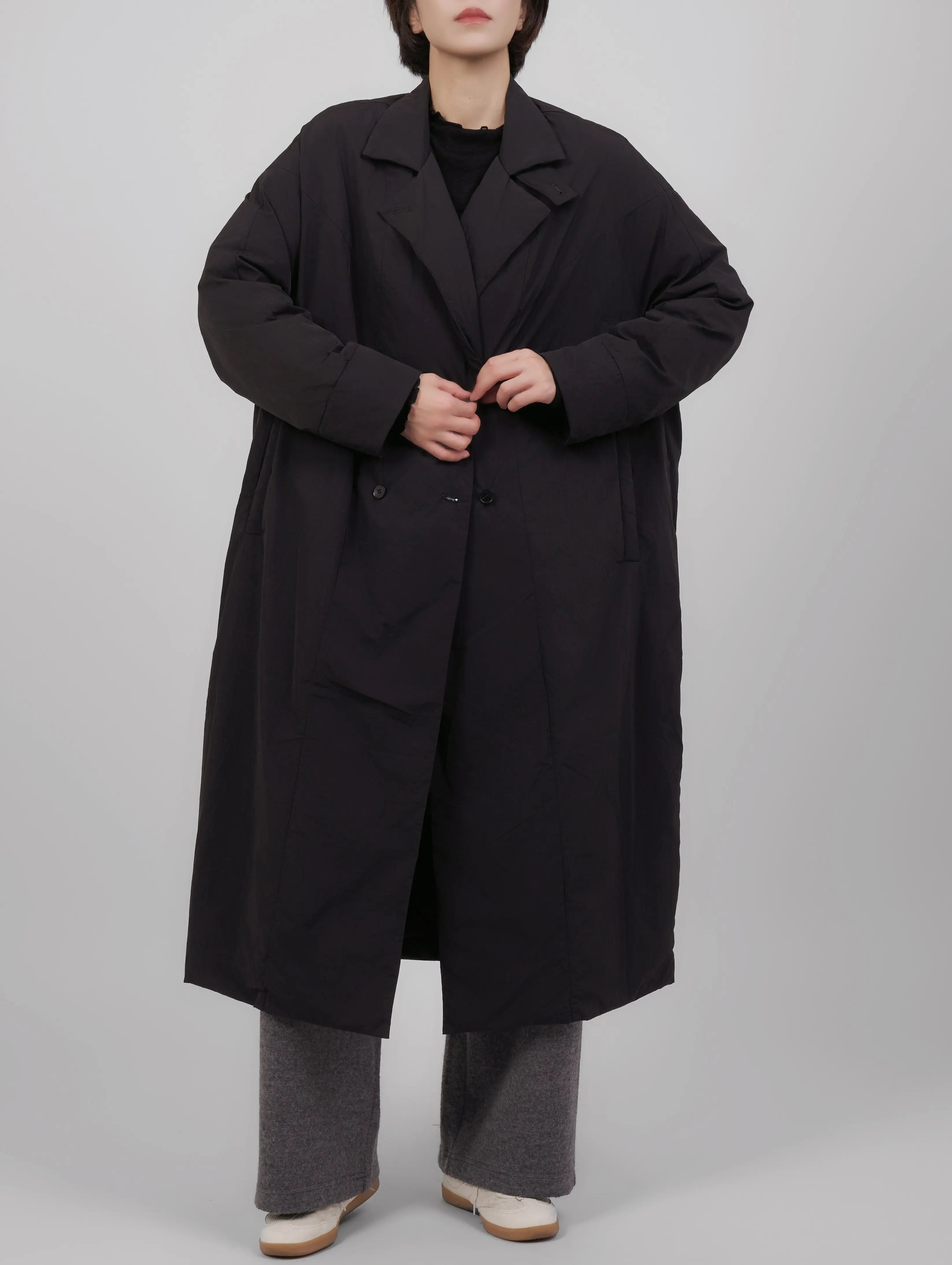 Full body look of a black oversized down coat styled with wide-leg trousers, showing a relaxed winter silhouette.