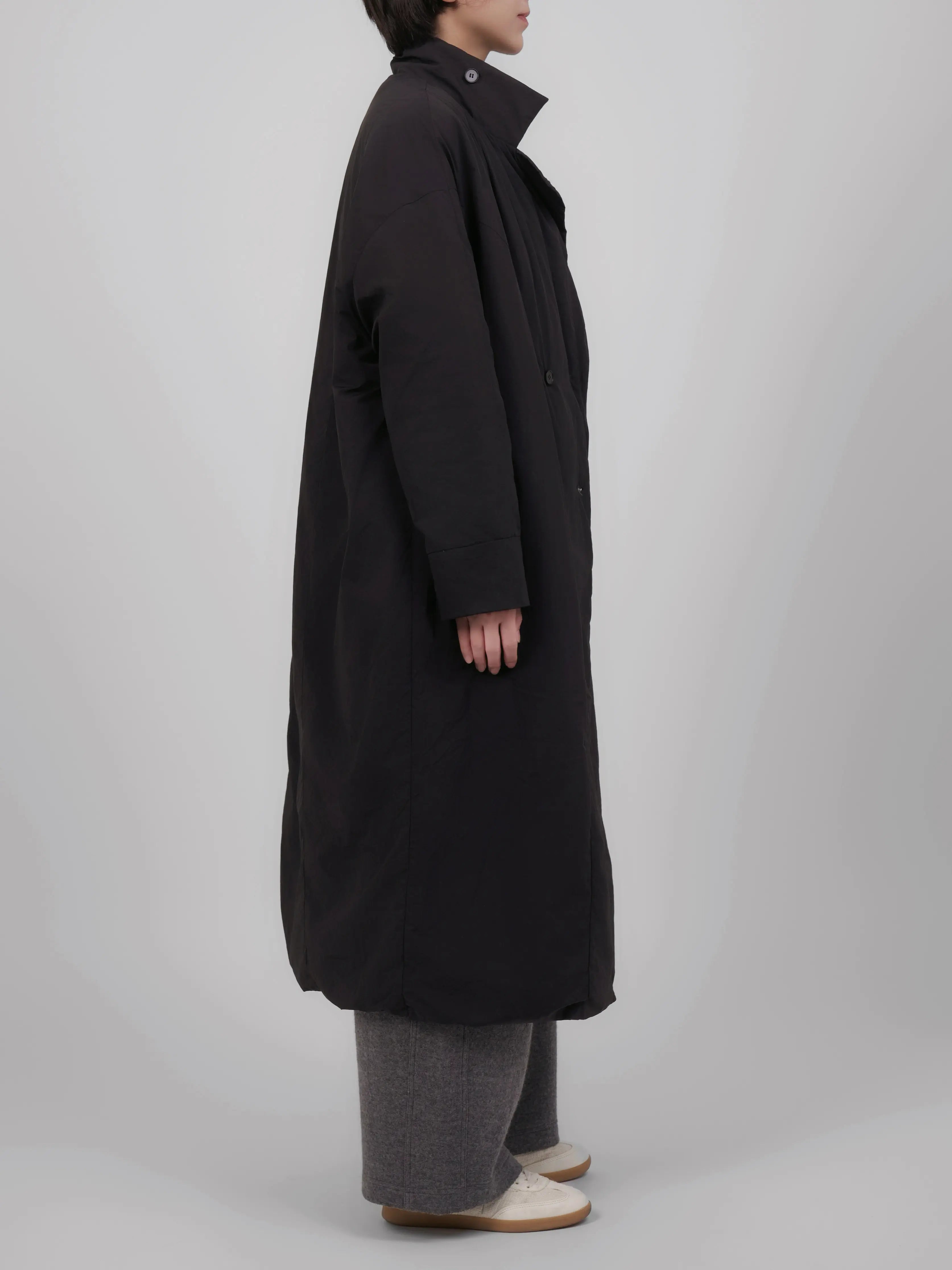 Side view of long black down coat emphasising length and relaxed proportions.