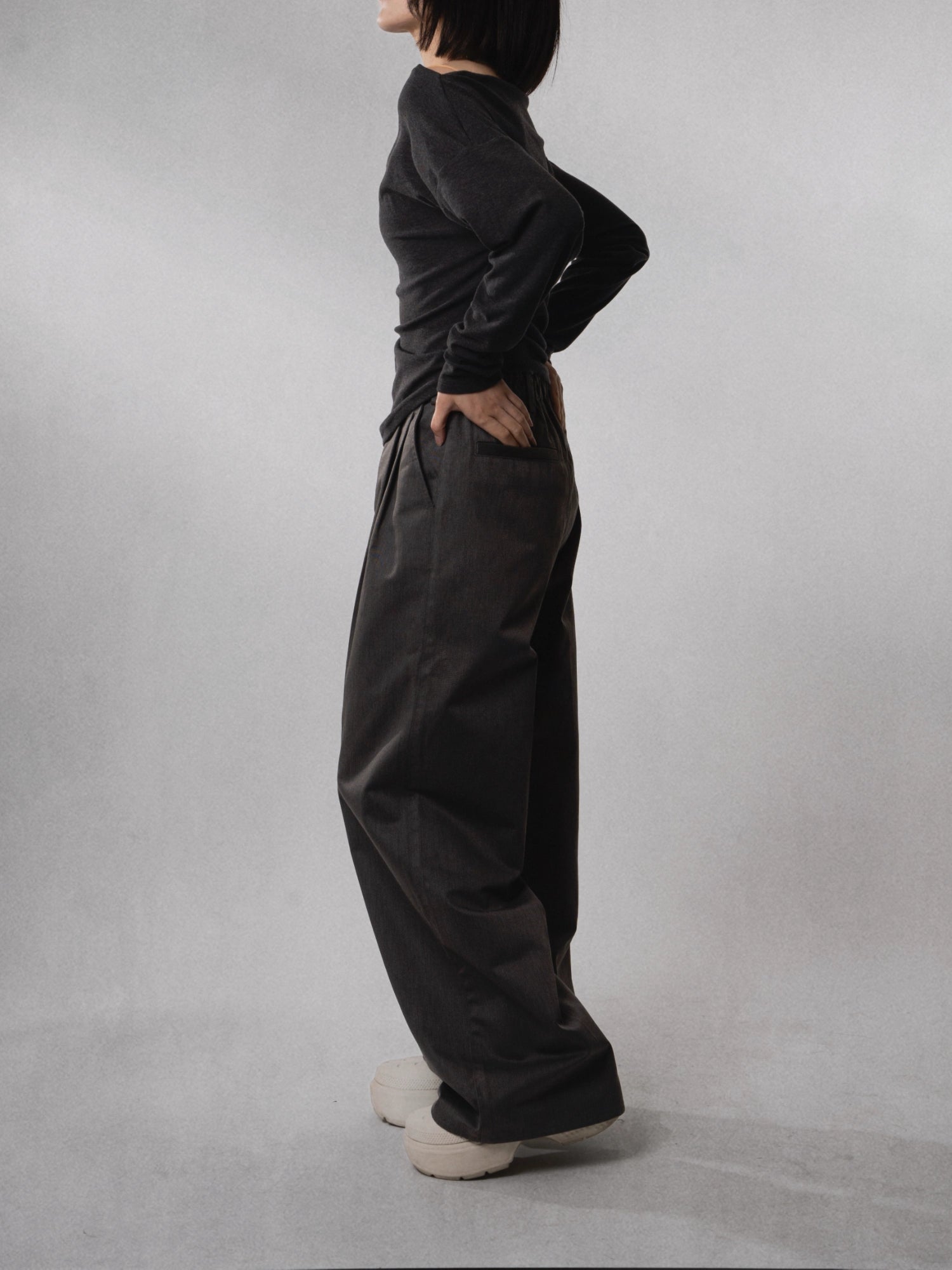 Side profile of drape wide-leg trousers, showing soft movement and relaxed high-rise fit.
