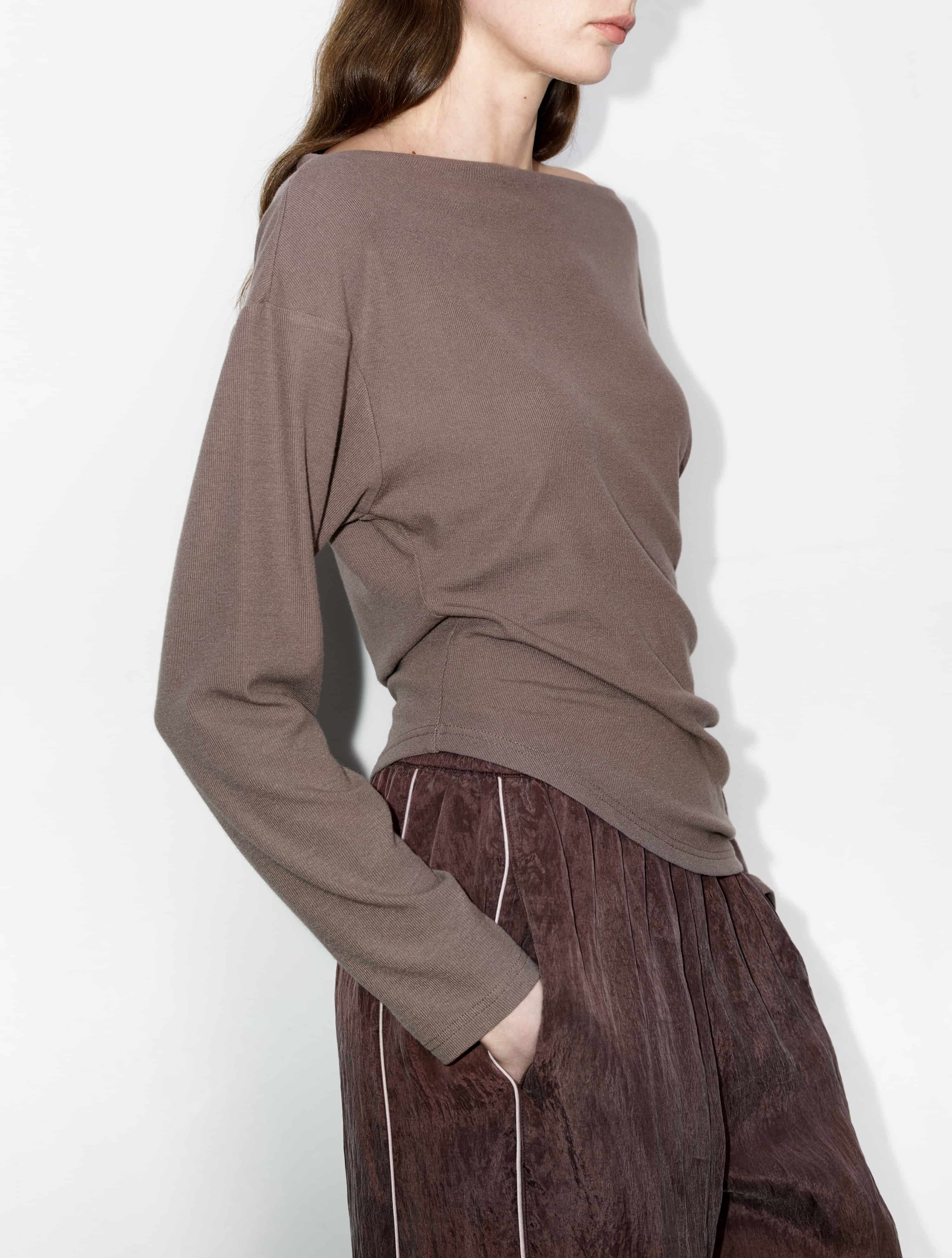 Back-angled shot of brown irregular hem top, lightweight year-round knit, styled with wide trousers, soft shoulder line.