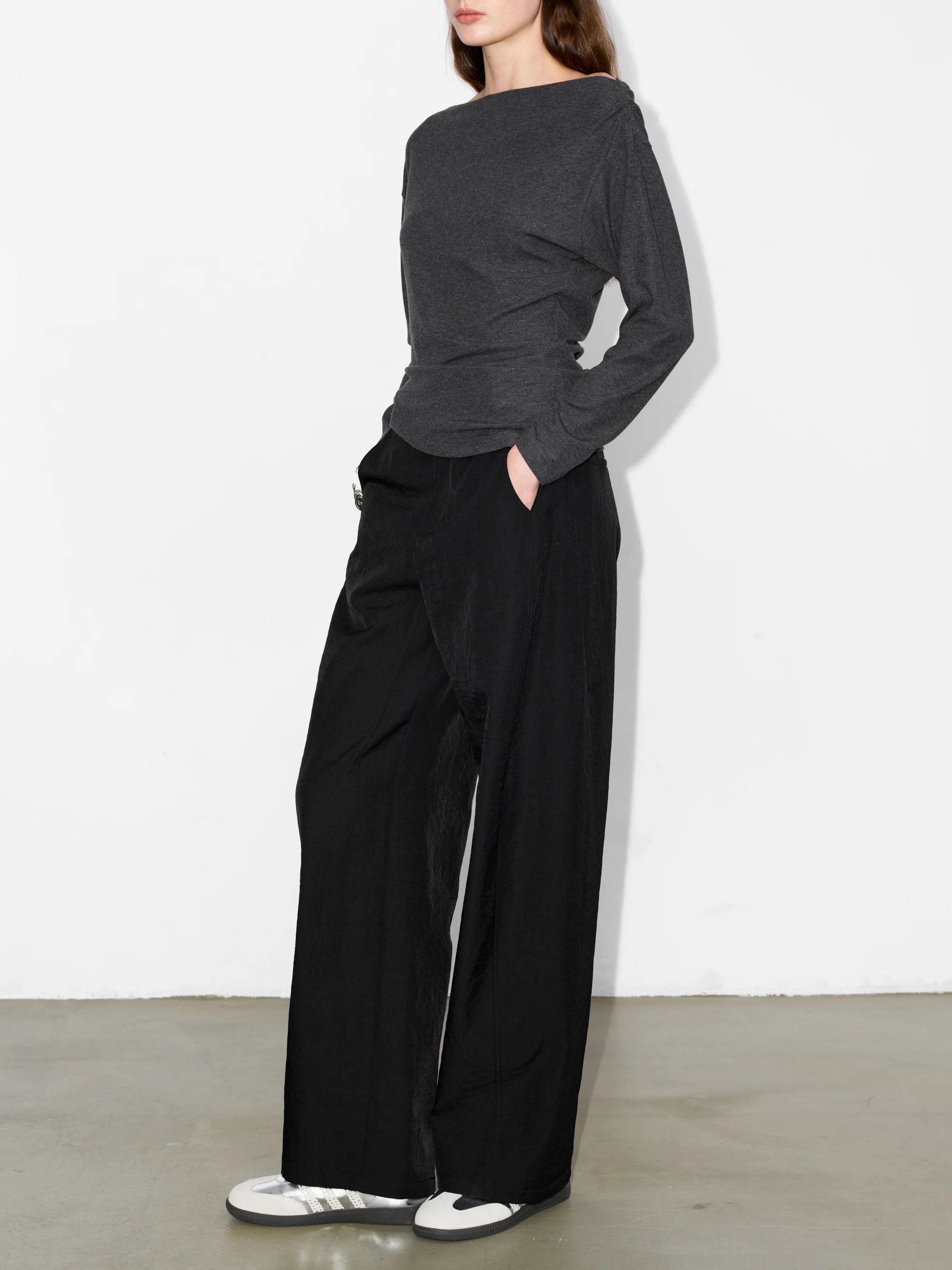 Full-body front view in grey irregular hem knit top, paired with black pants, showing natural drape and asymmetric neckline.