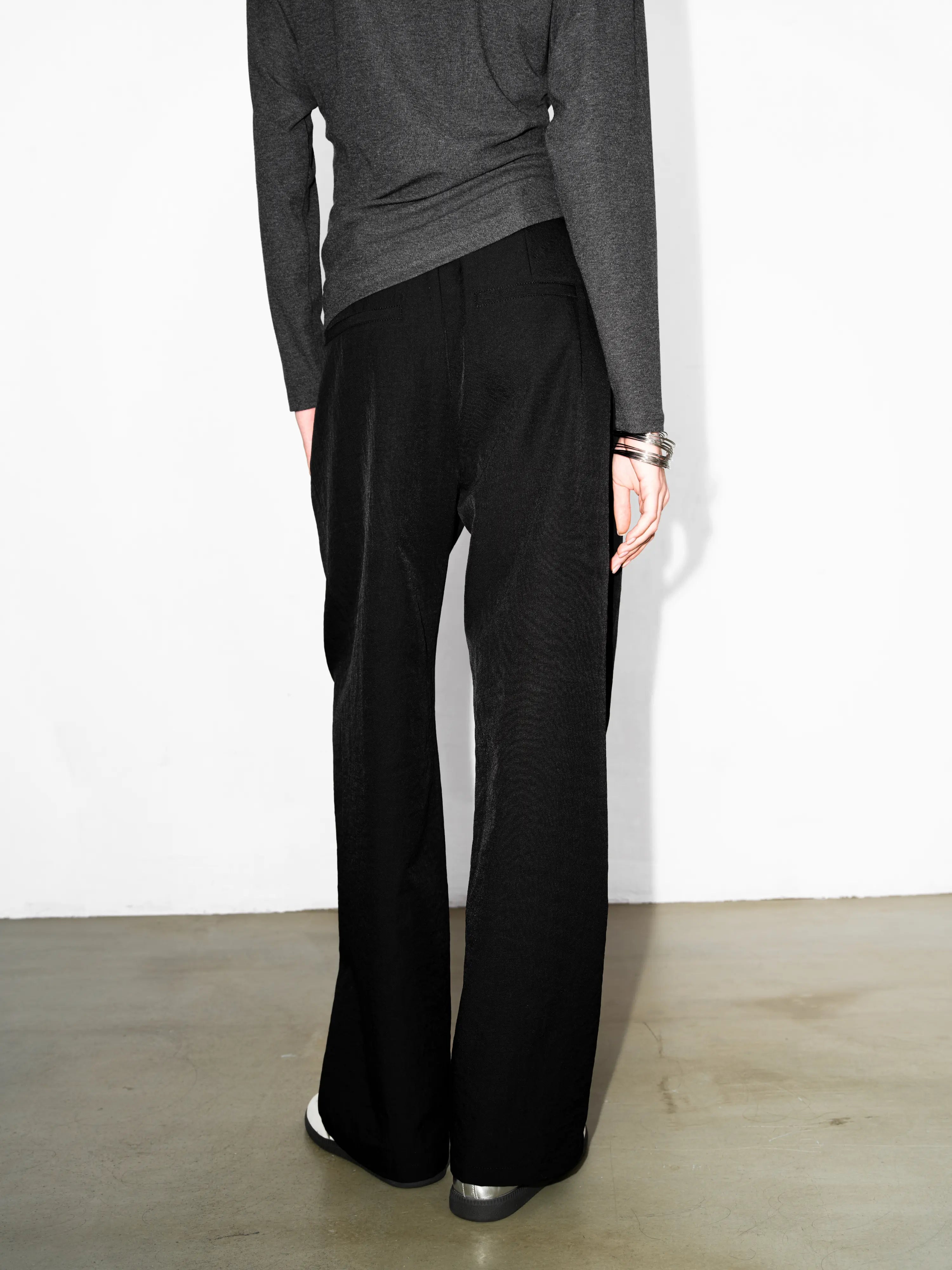 Side angle of black cocoon trousers showing relaxed leg shape and soft drape, styled with knit top for minimal city outfits.