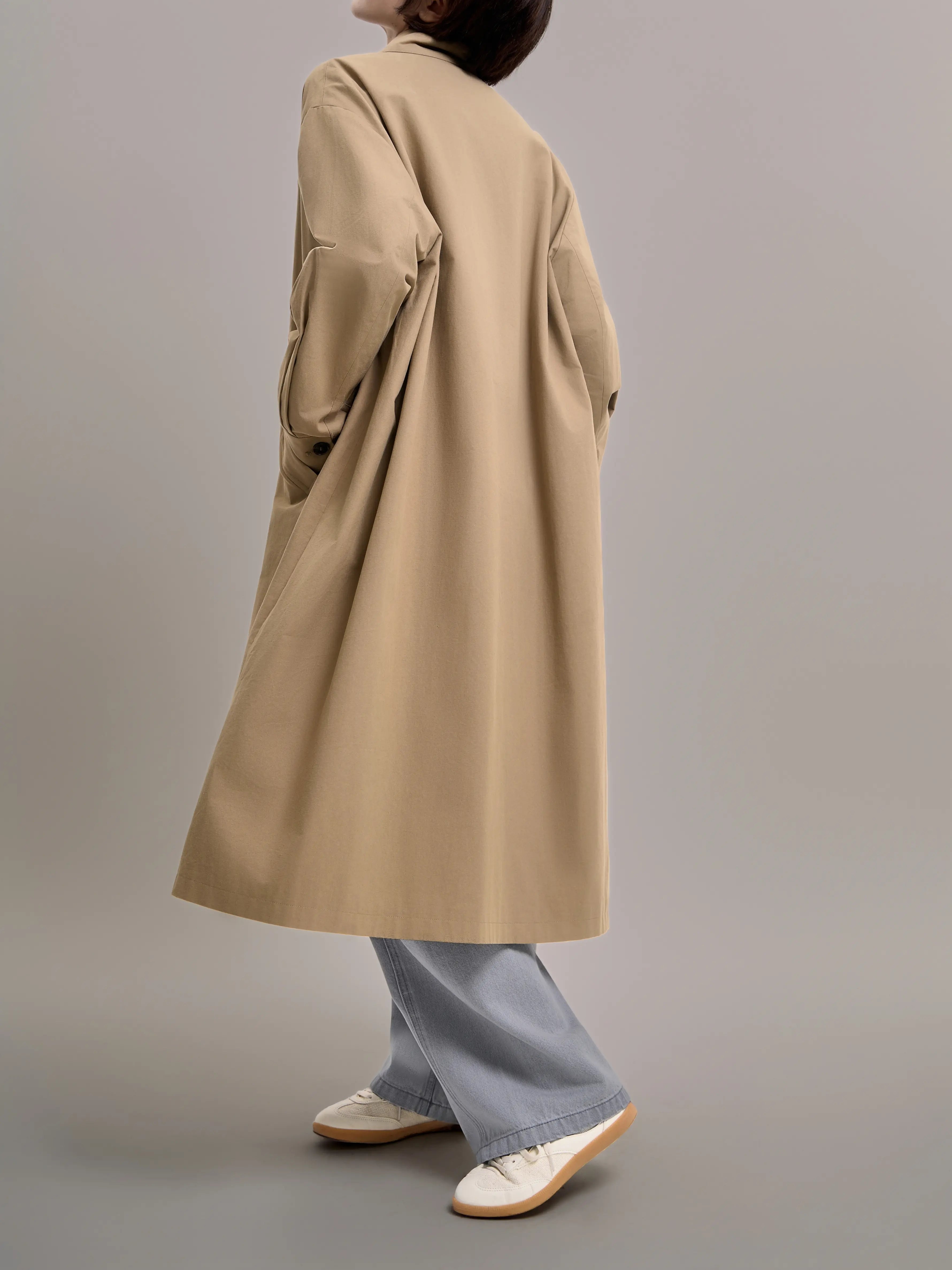Back view of khaki trench coat featuring an oversized silhouette, emphasizing clean lines and structured minimal design.