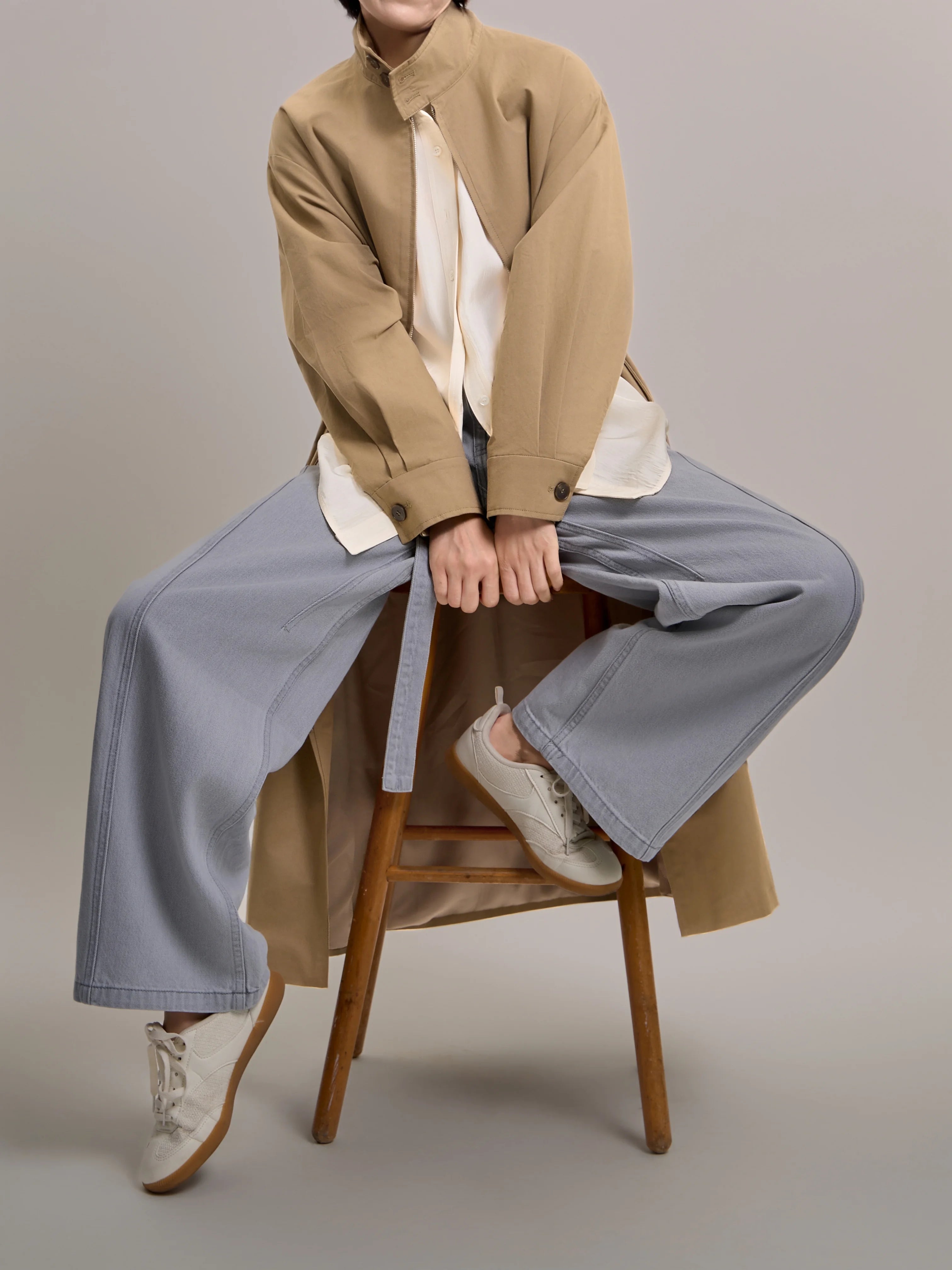 Lifestyle shot of khaki trench coat worn in a relaxed seated pose, showing effortless minimal styling and comfort.