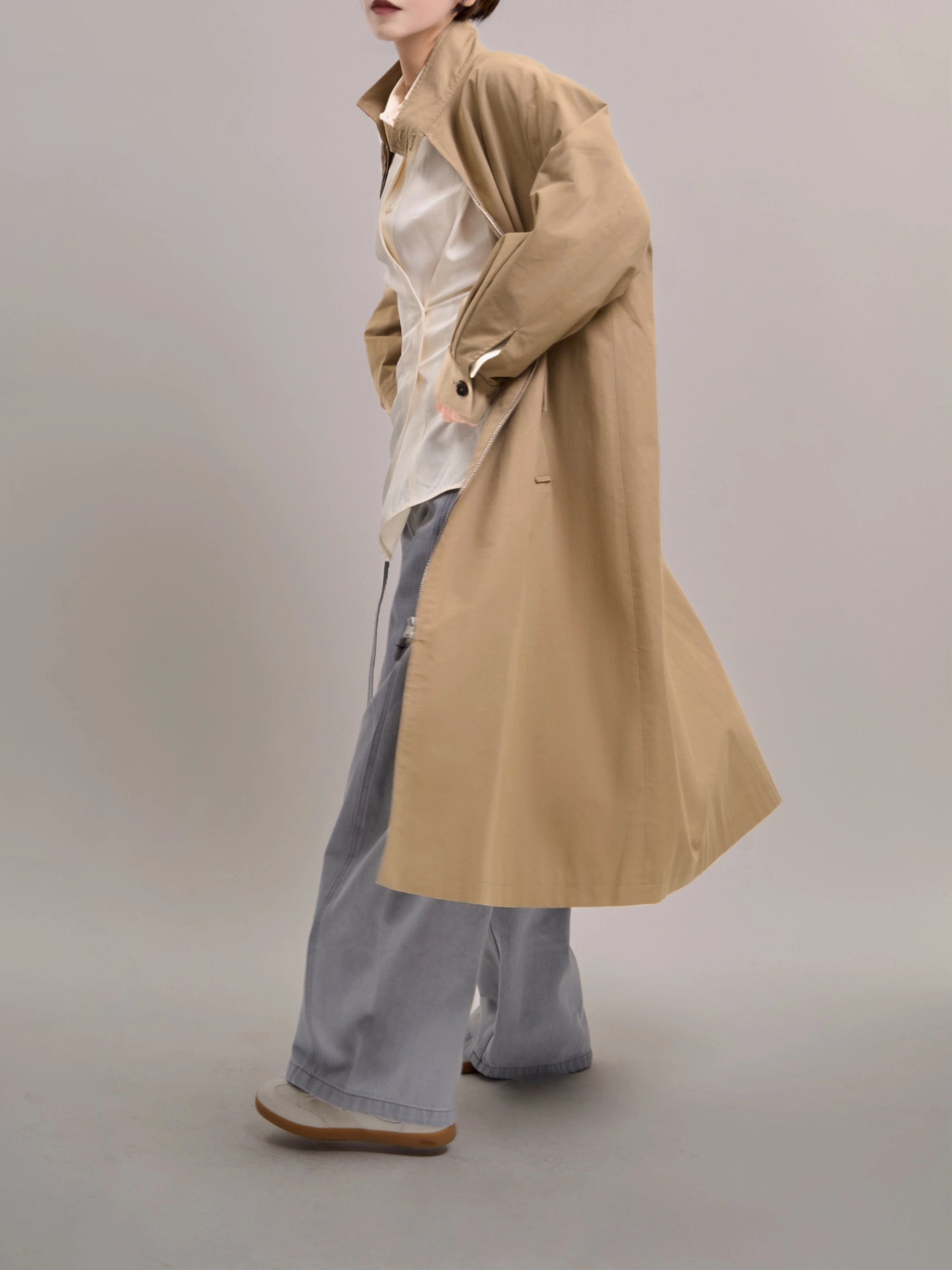 Walking motion shot of khaki trench coat, highlighting the natural movement and long relaxed silhouette.