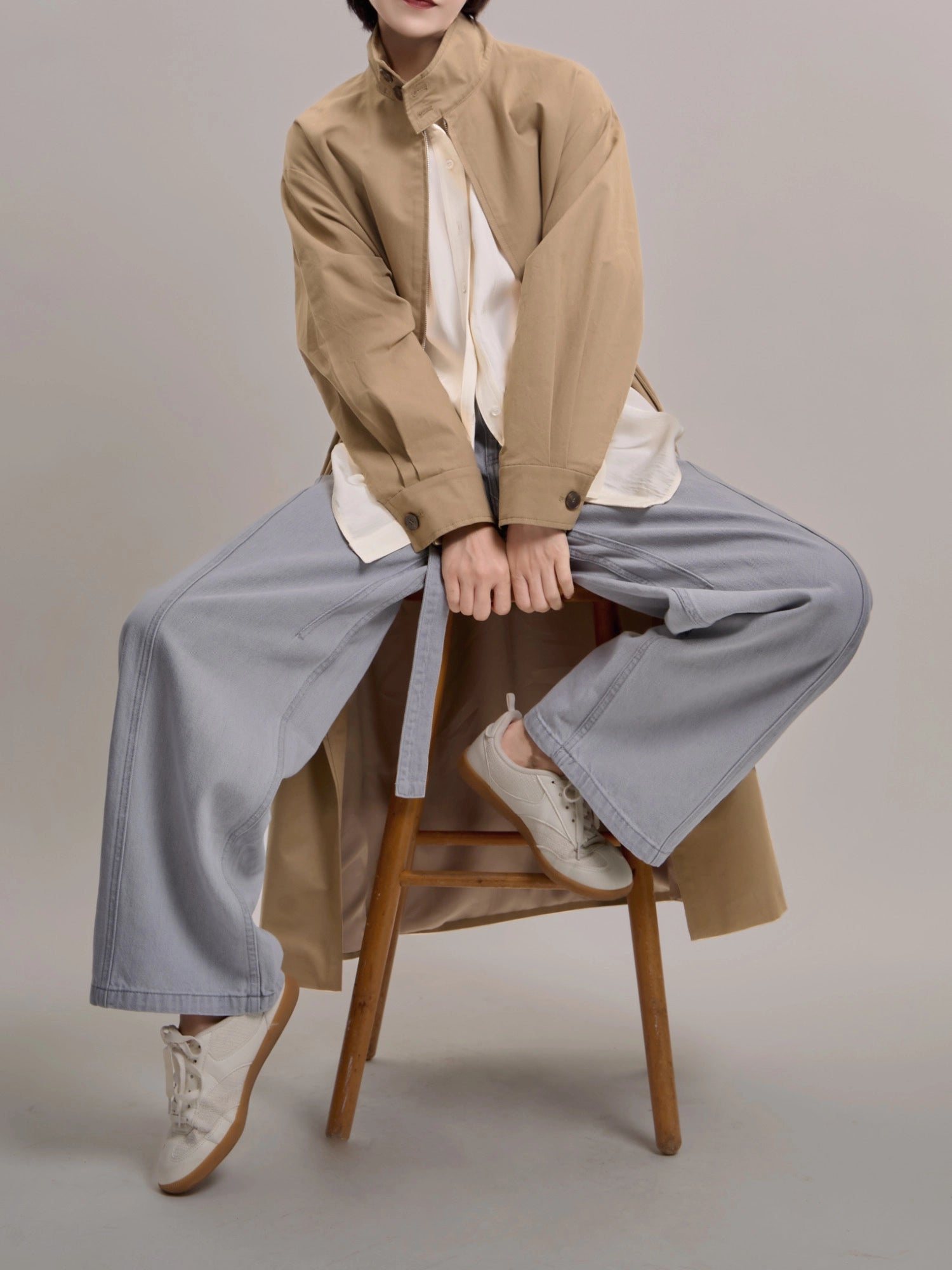 Seated styling of khaki trench coat, showing relaxed layering and breathable cotton texture.