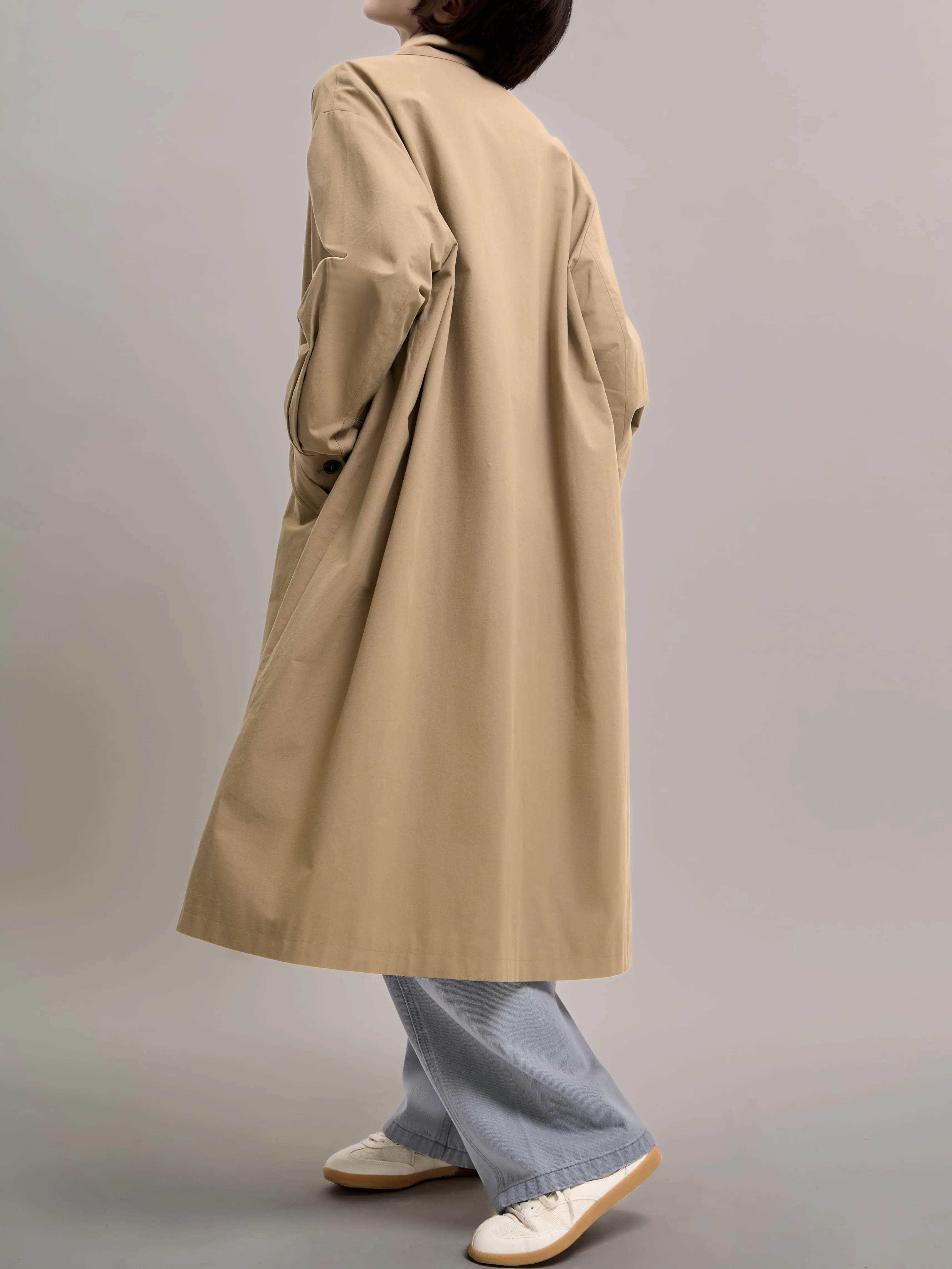 Side profile of khaki cotton trench coat, highlighting the long straight silhouette and clean minimalist lines.
