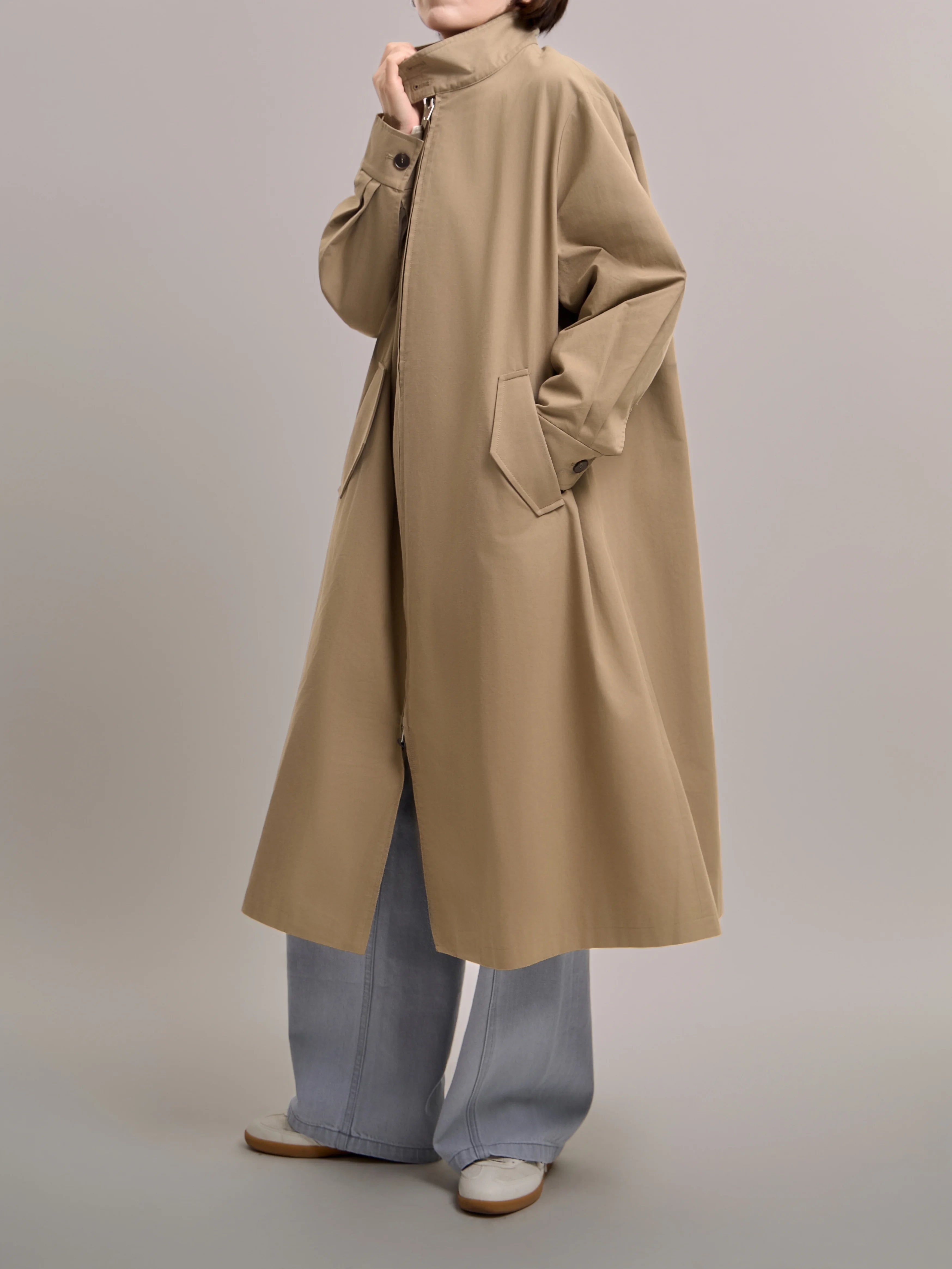 Side view of khaki trench coat in motion, highlighting the relaxed silhouette and fluid drape in a minimalist city look.