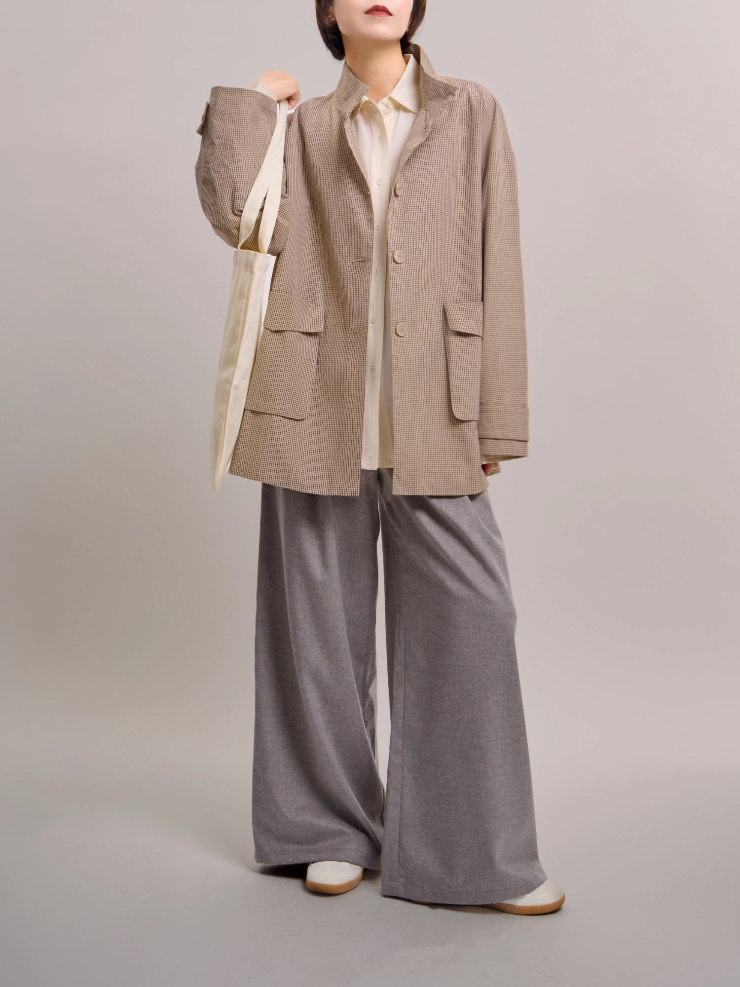 Beige minimal check jacket styled with tote bag and trousers, showing versatile everyday layering.
