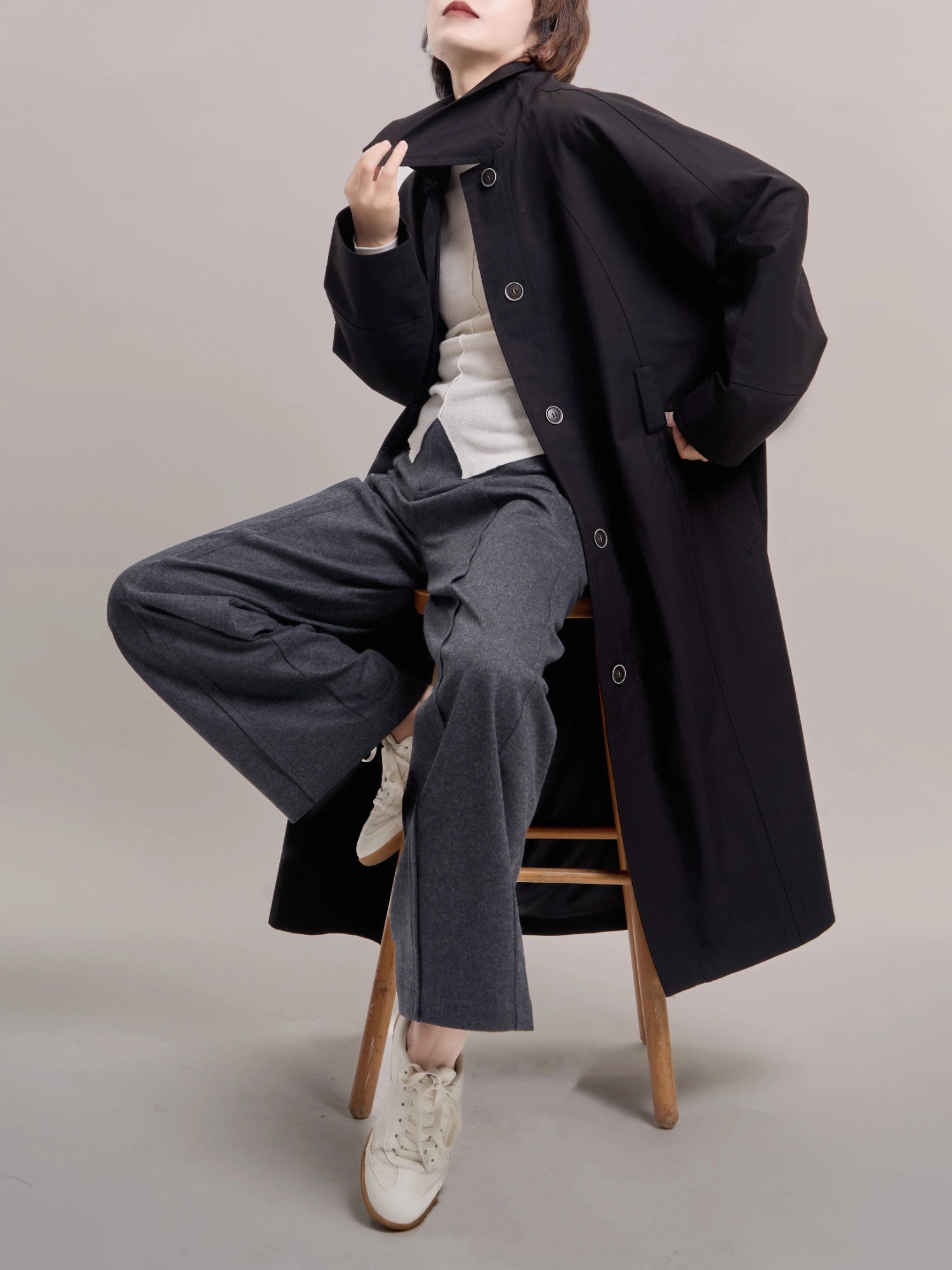 Seated styling of black Noir Trench, highlighting relaxed movement and fluid silhouette.