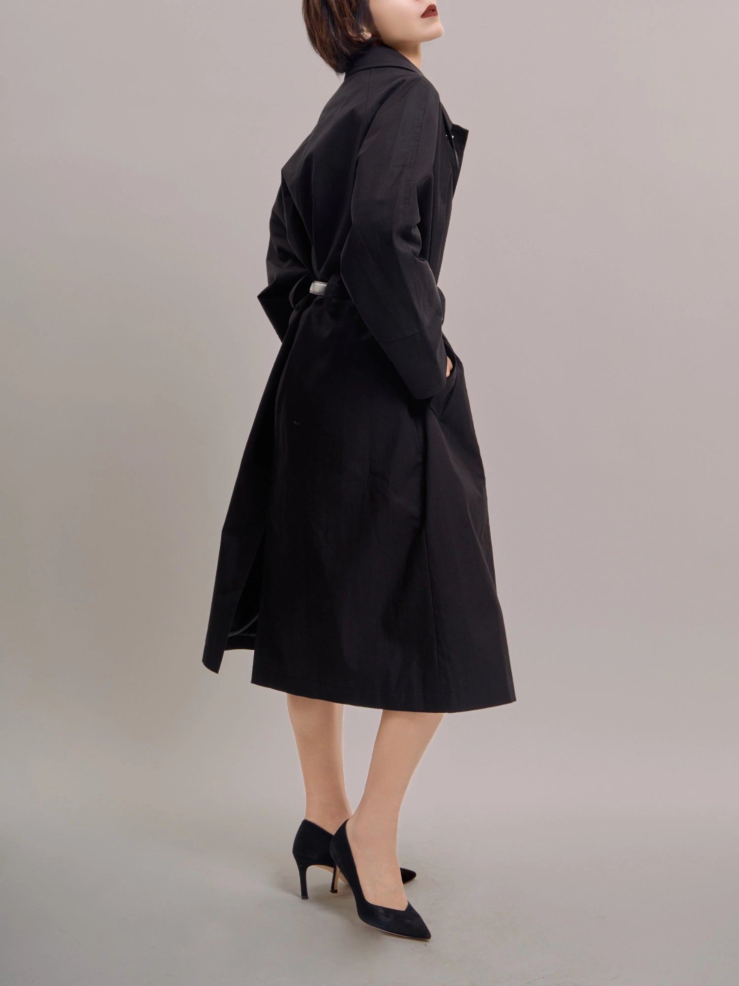 Side profile of black Noir Trench showing fluid drape and relaxed batwing sleeve shape.