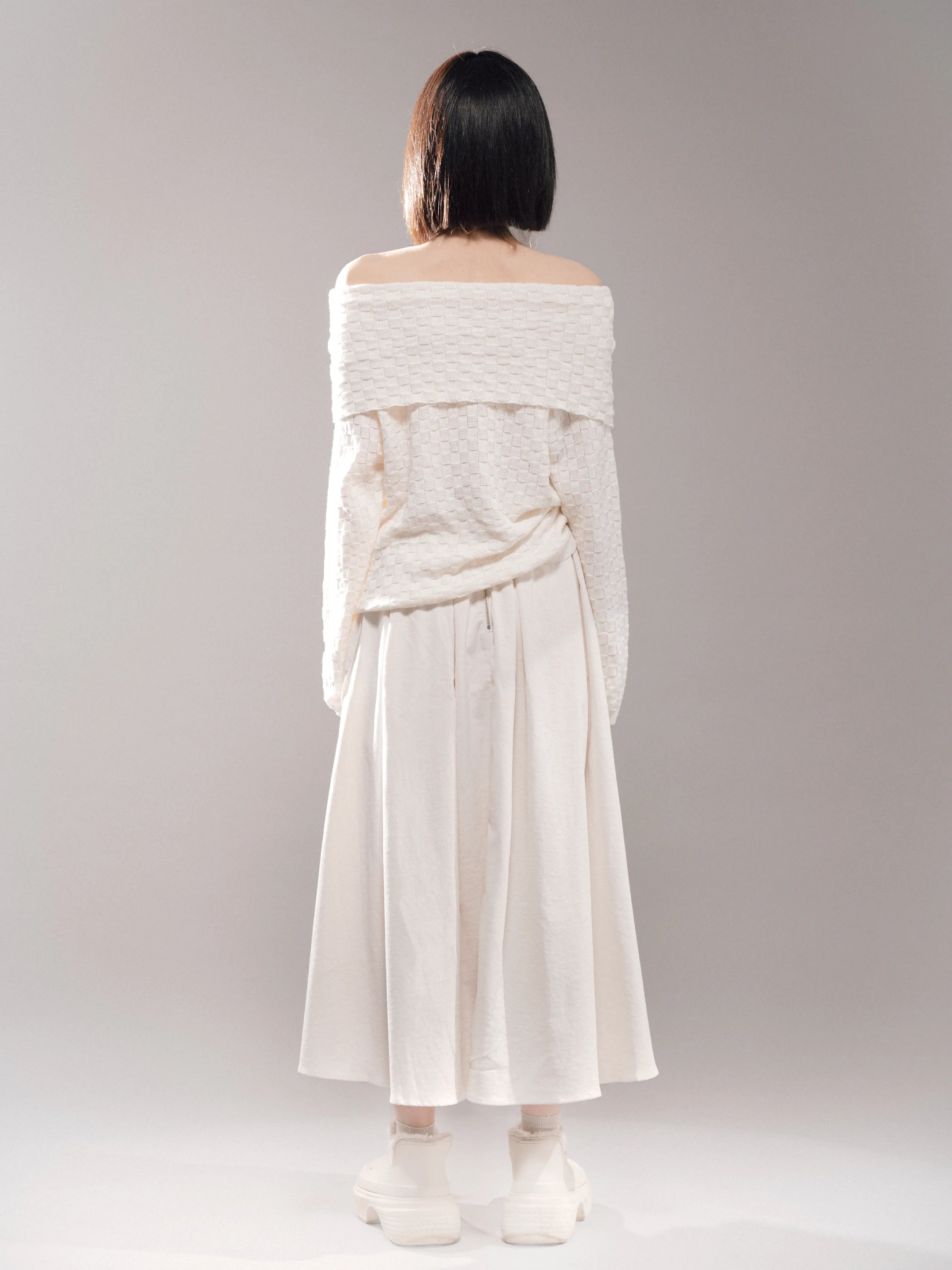 Back view of white off-shoulder top, long sleeves, soft knitted texture, styled with flowing skirt for clean minimalist outfit.

