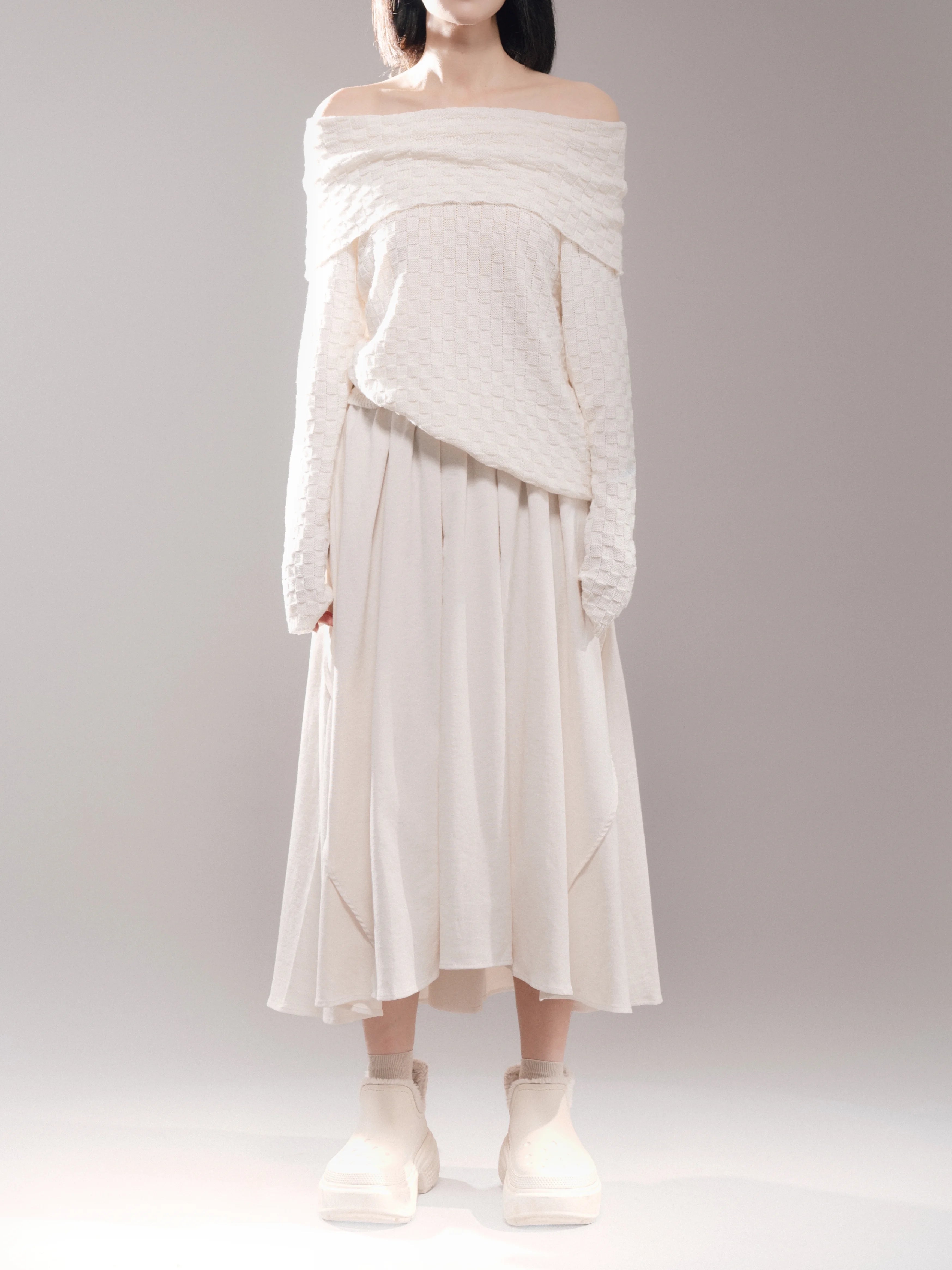 White off-shoulder top full body front view, soft drape sweater paired with cream skirt, minimal styling for editorial product display.
