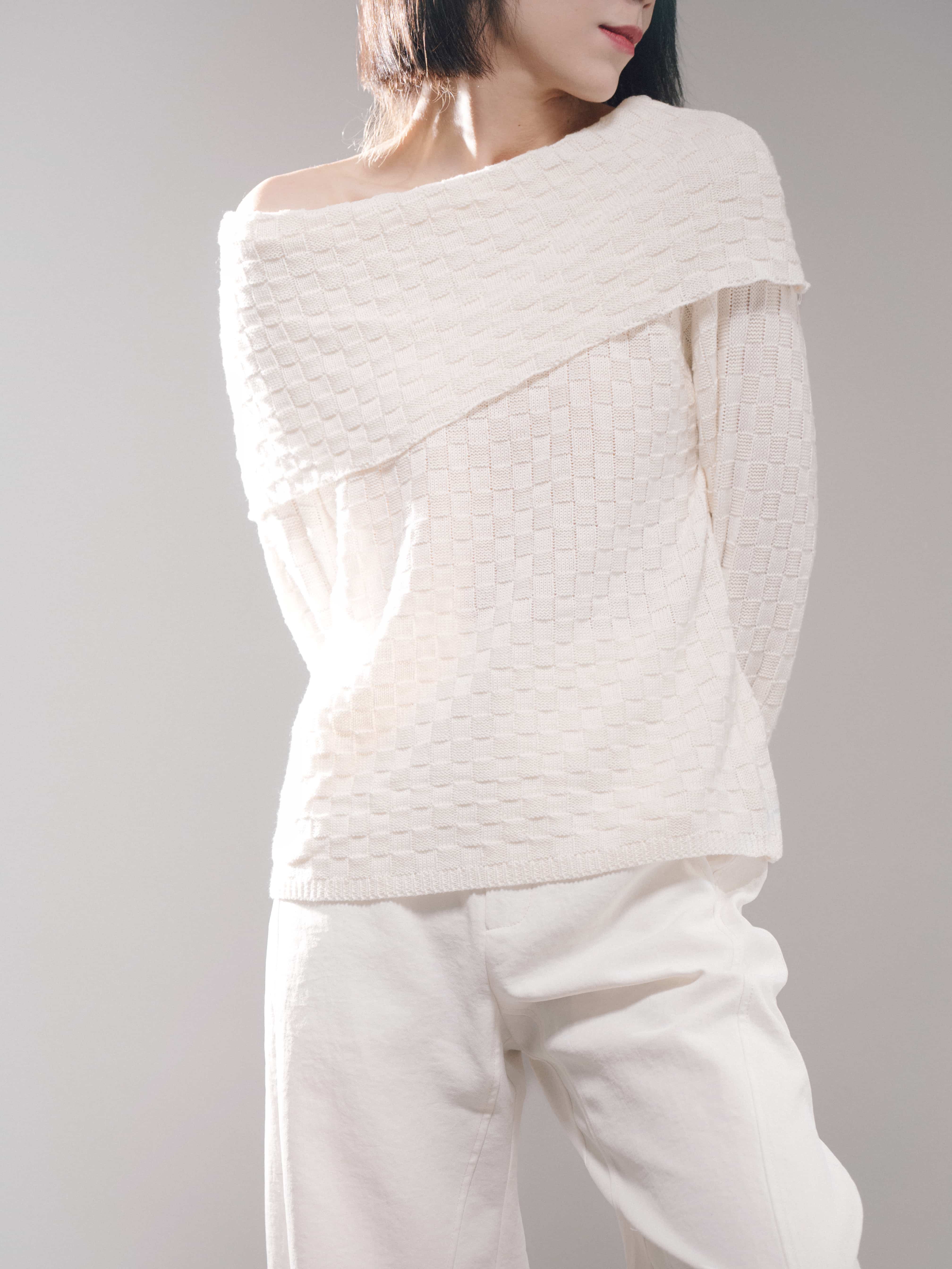 Side angle detail of white off-shoulder knit top, relaxed drape, clean neckline, lightweight cozy texture in soft lighting.
