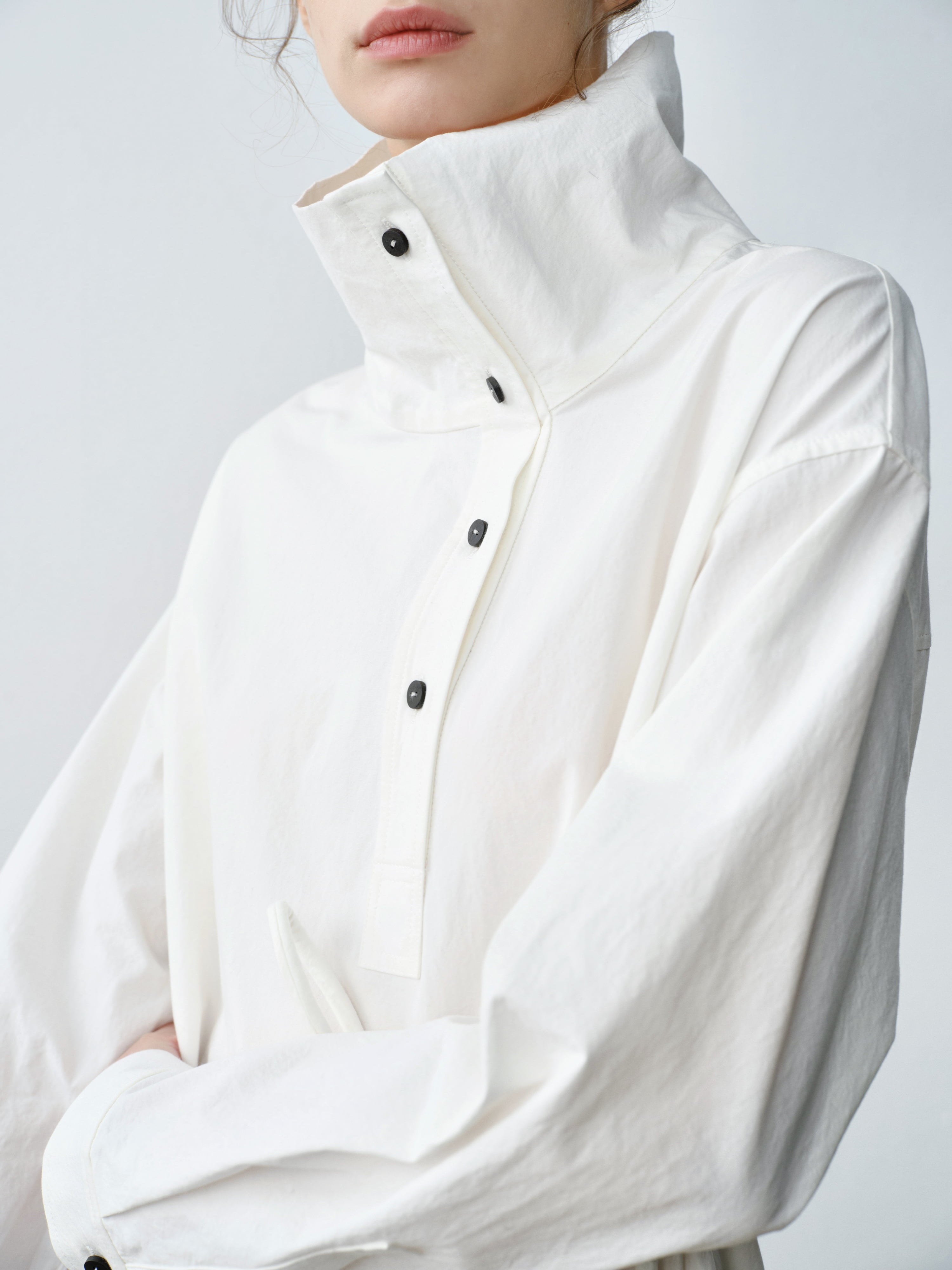 Close-up of structured stand collar and button fastening on white Pima cotton dress, clean modern aesthetic.