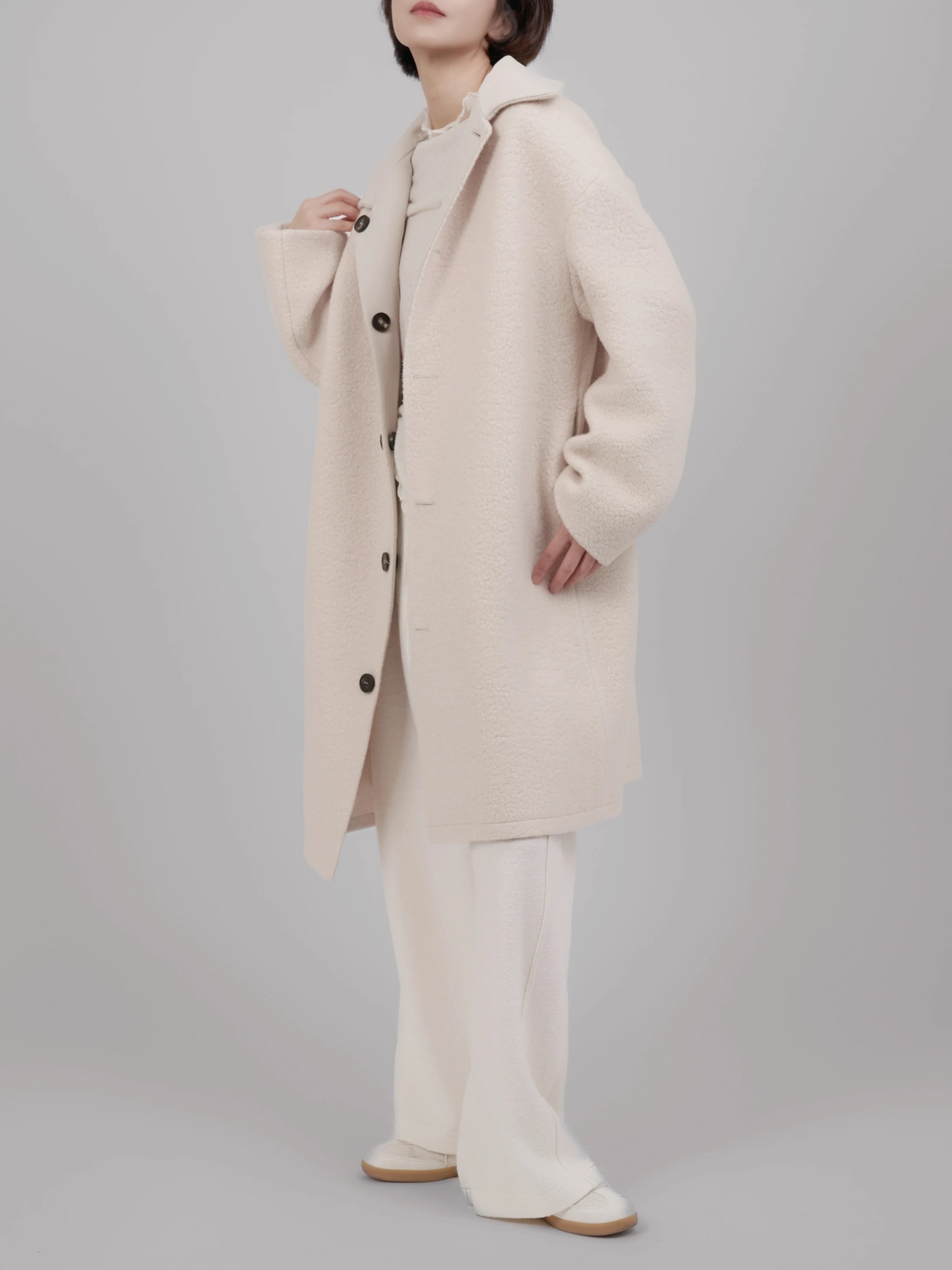 Full body look of a beige reversible wool coat styled with wide-leg trousers, showing a relaxed minimalist silhouette.