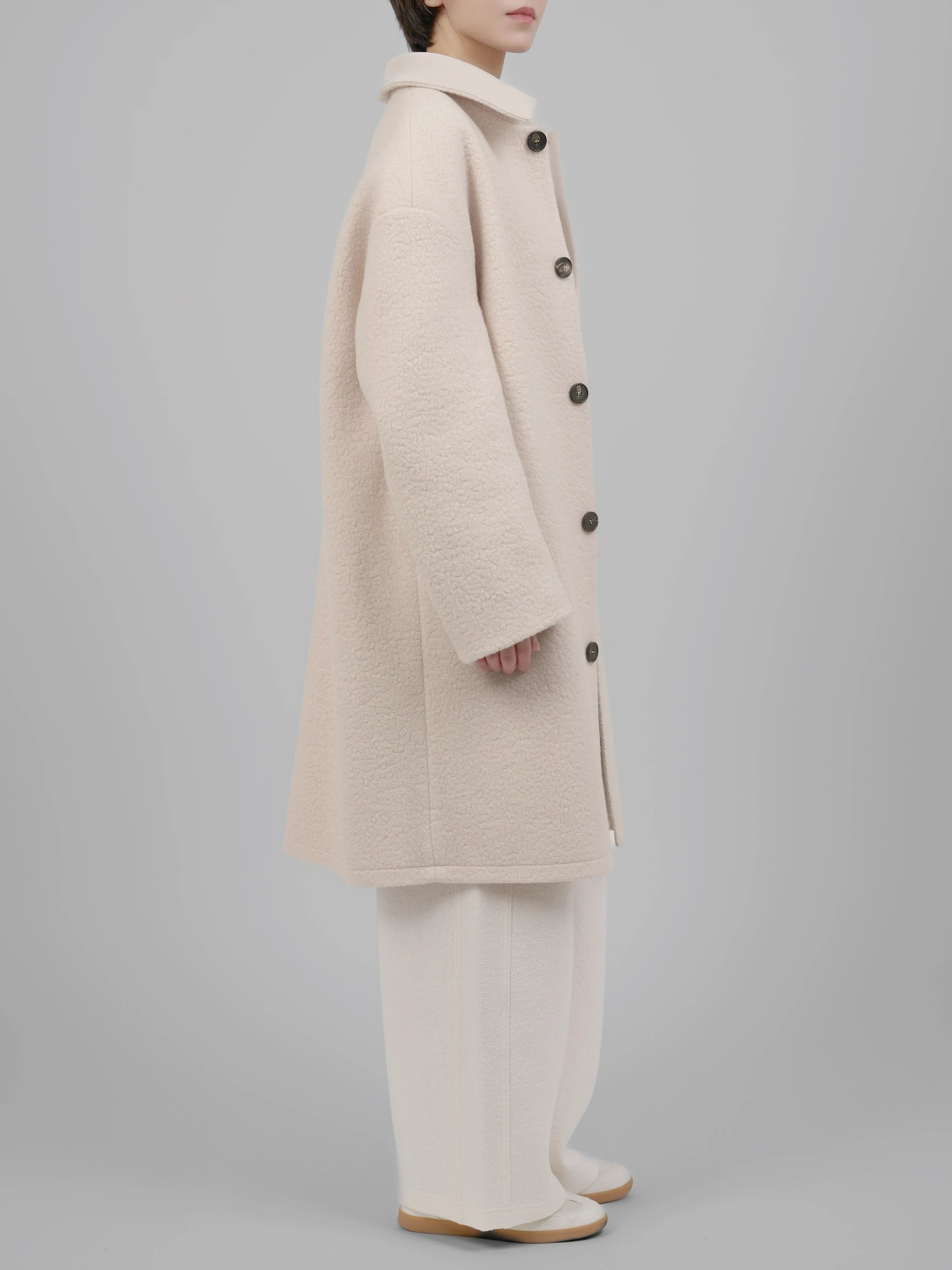 Side view of beige wool coat highlighting its loose structure and effortless drape.