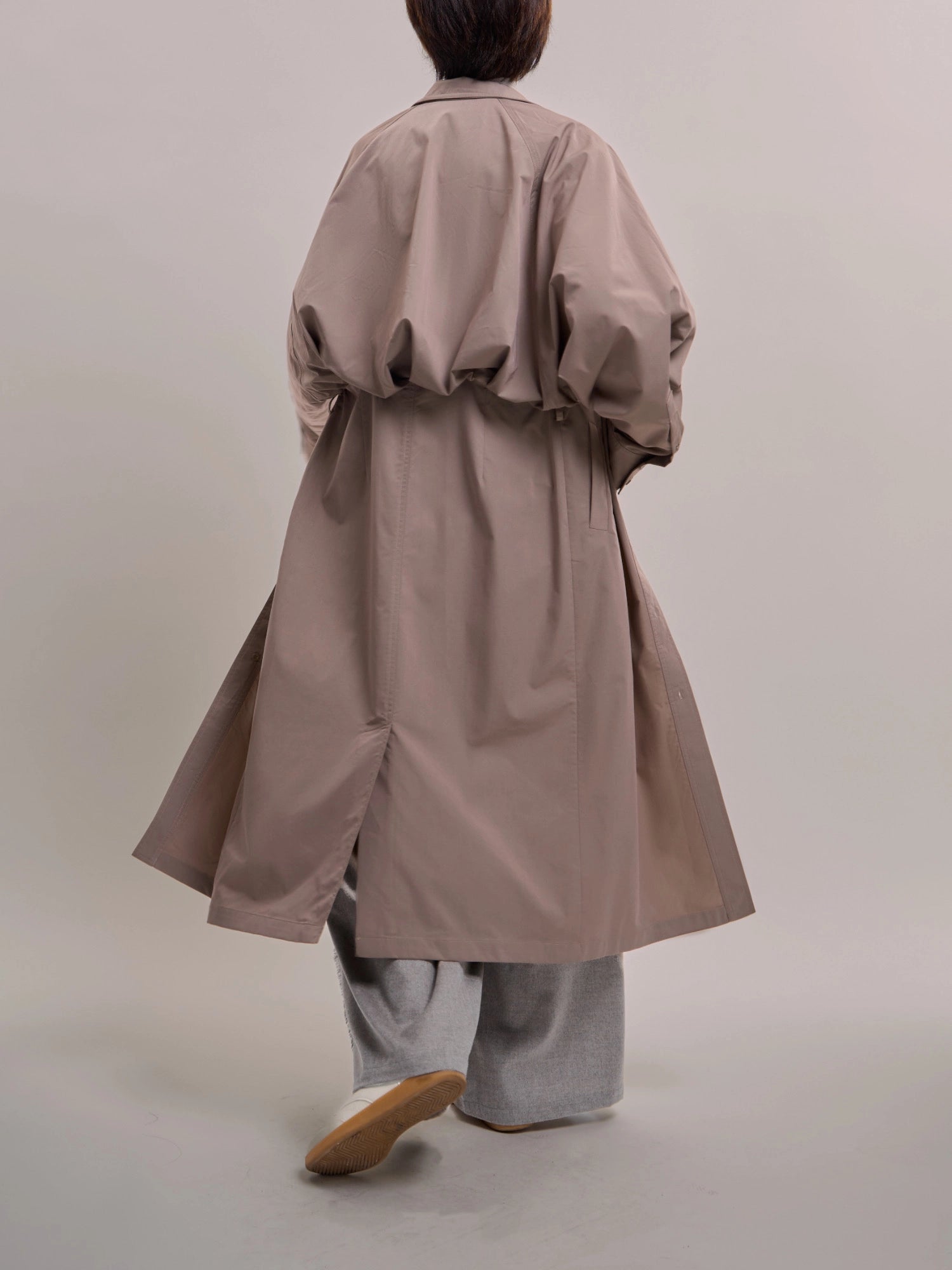 Back view of taupe Ripple Trench featuring gathered back construction and long fluid hem.