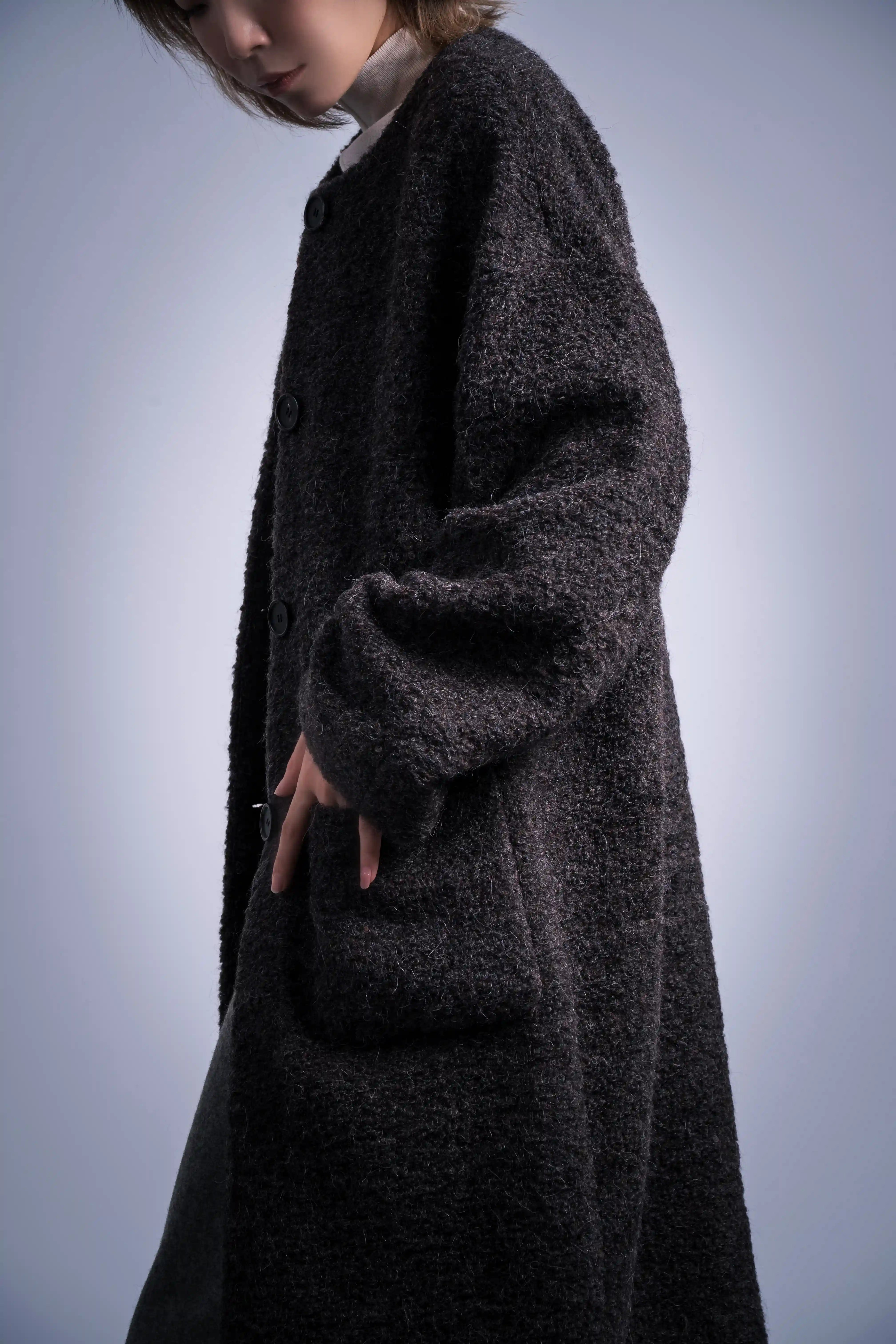 Side profile close detail of charcoal wool coat, soft texture, dropped shoulder line, minimal styling.
