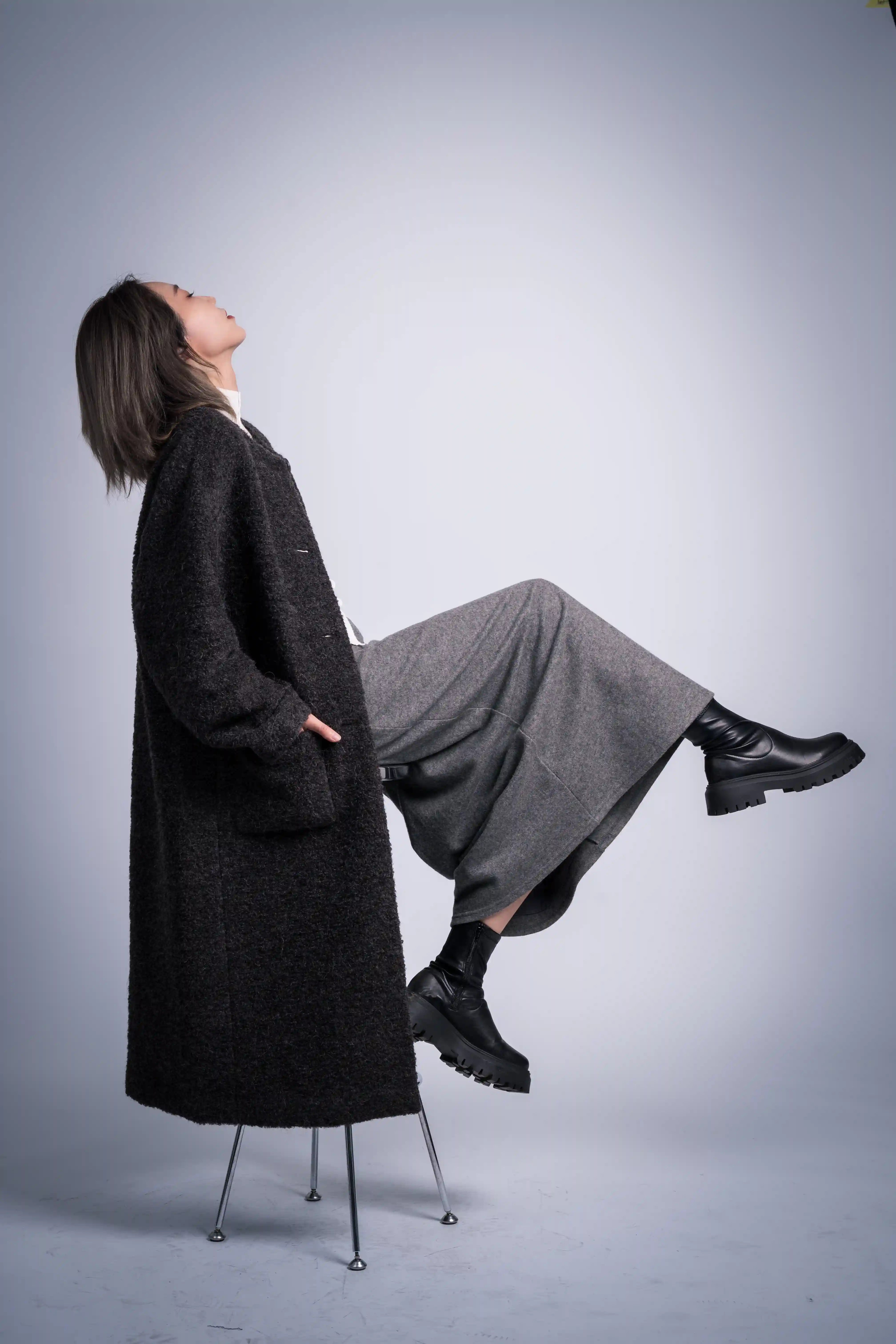 Model seated in charcoal alpaca wool coat, editorial pose, soft structured silhouette, winter outerwear styling.