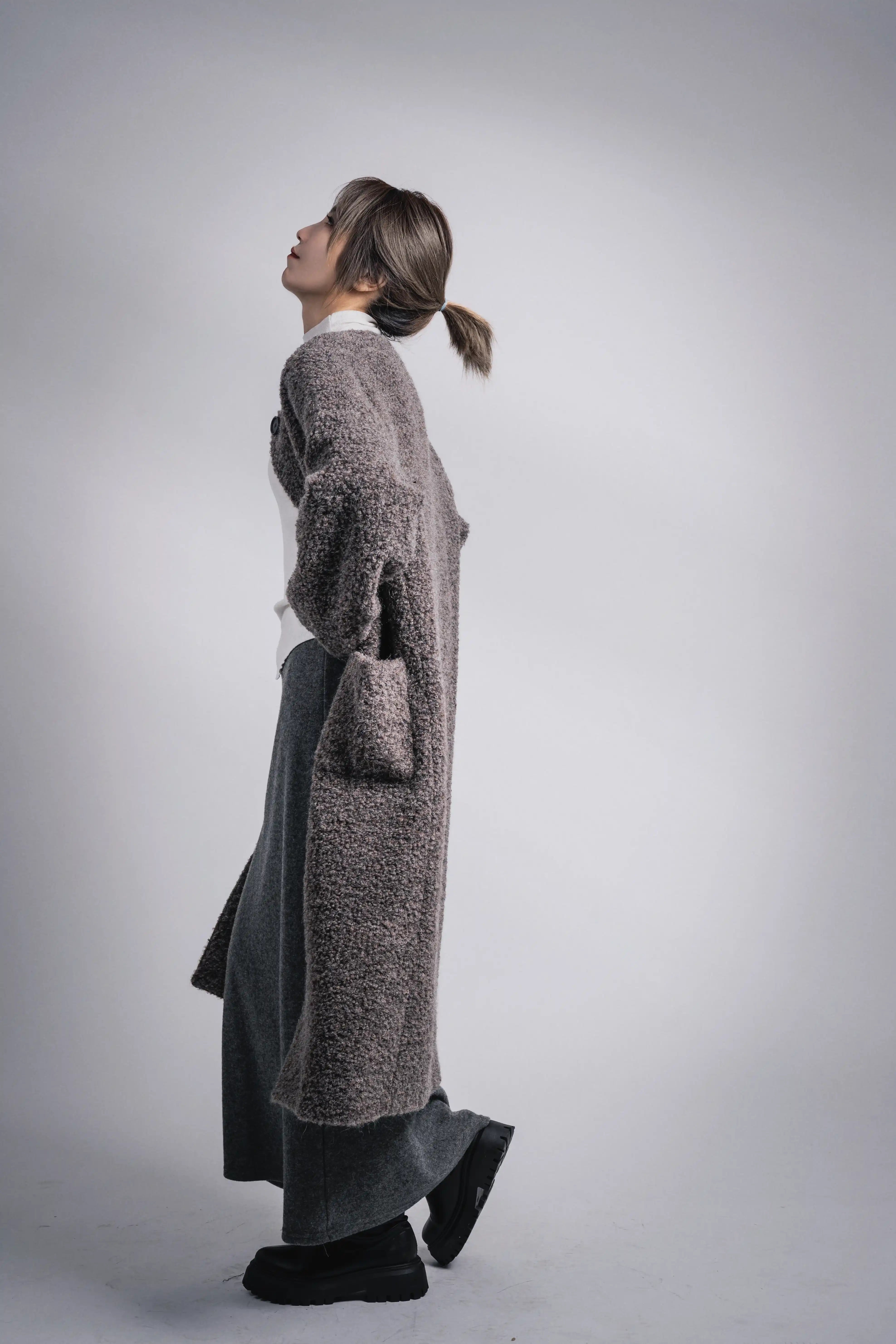 Grey wool alpaca coat side profile, hands in pockets, relaxed modern winter silhouette.
