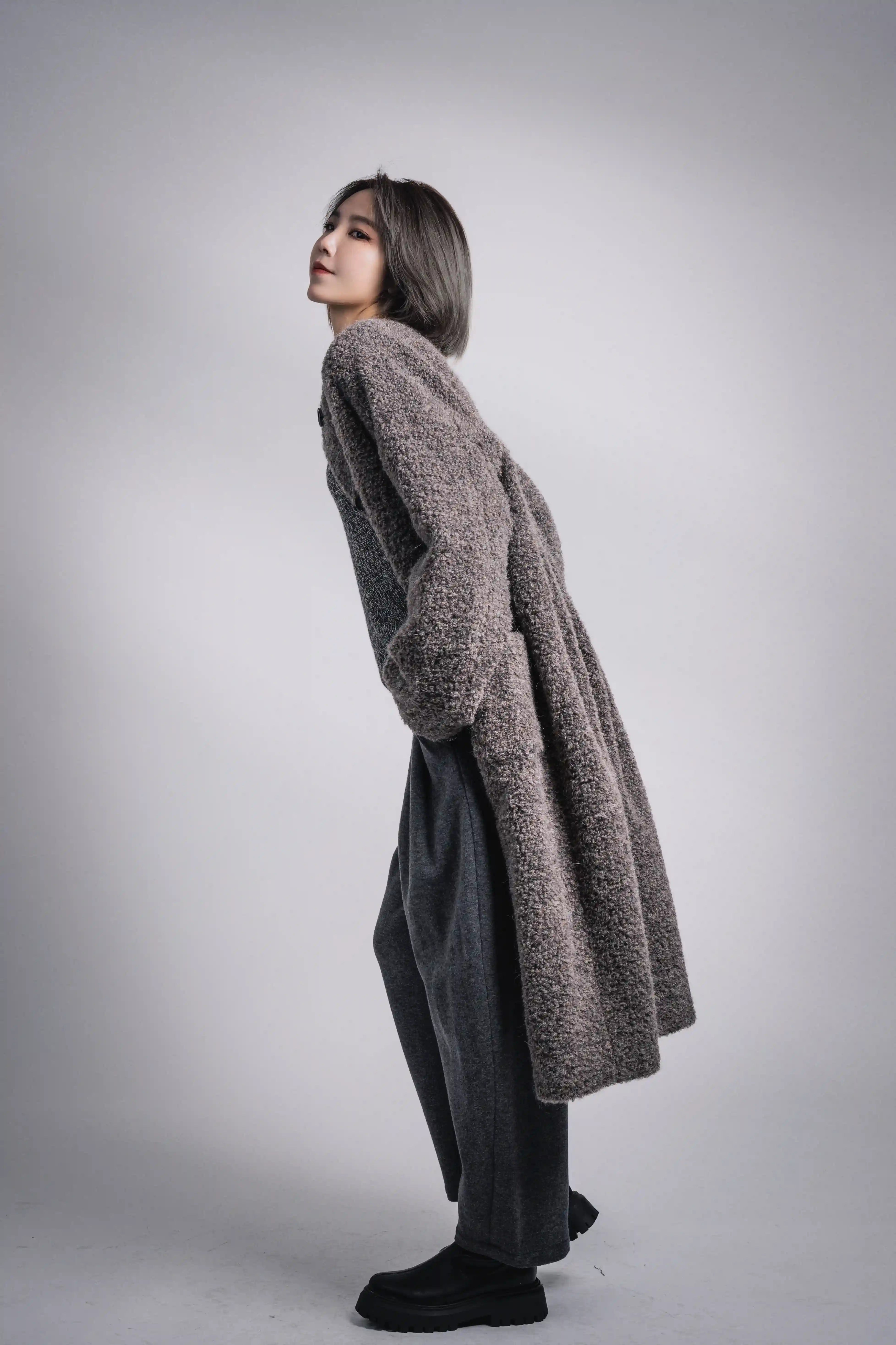 Side view of grey Snowy Grace alpaca wool coat, long slim silhouette paired with dark skirt and boots.