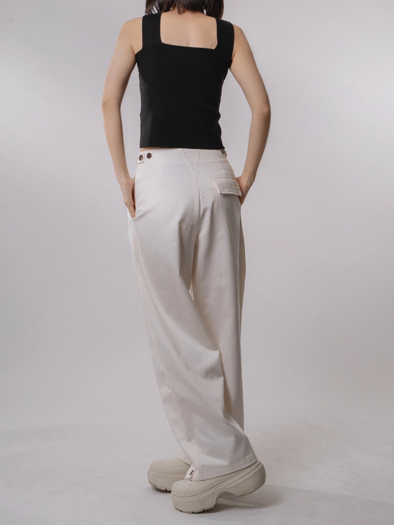 Front standing view of white loose-fit wide-leg trousers, clean pleats and long elongated line, paired with black top.