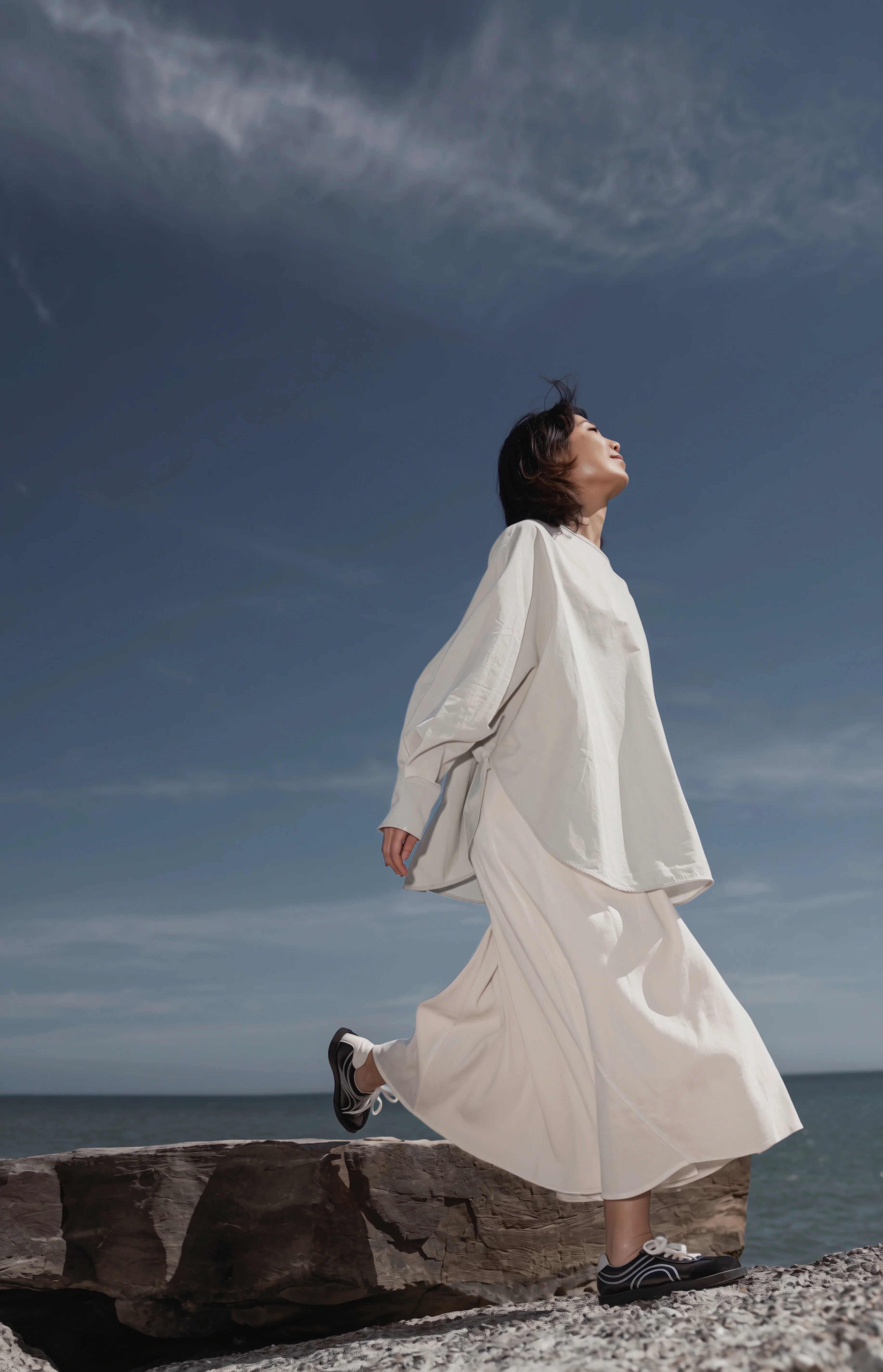 Model wearing the Batwing Pullover in Sage by the seaside, showcasing the flowing oversized silhouette.