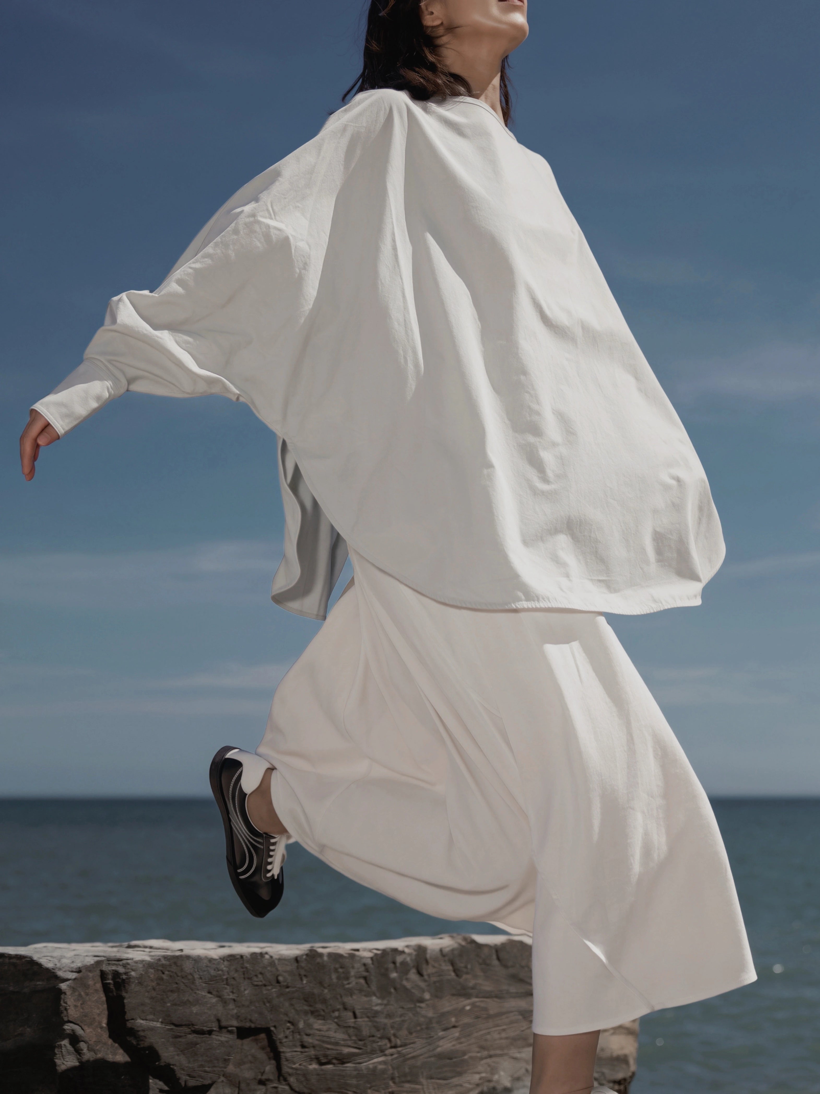 Model wearing the Batwing Pullover in Sage by the seaside with flowing movement.