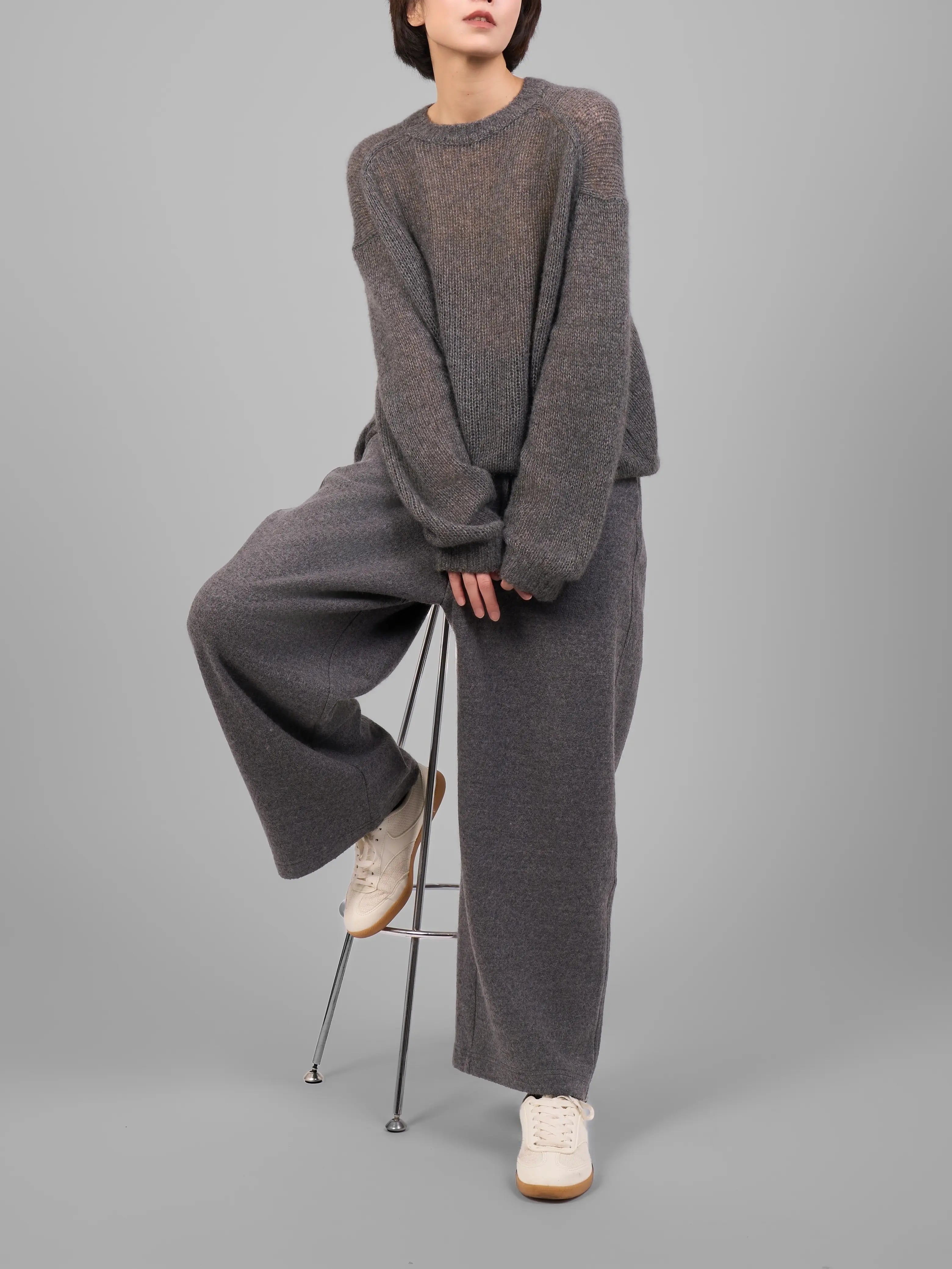 Model seated wearing grey cashmere-silk knit sweater and trousers in studio pose.