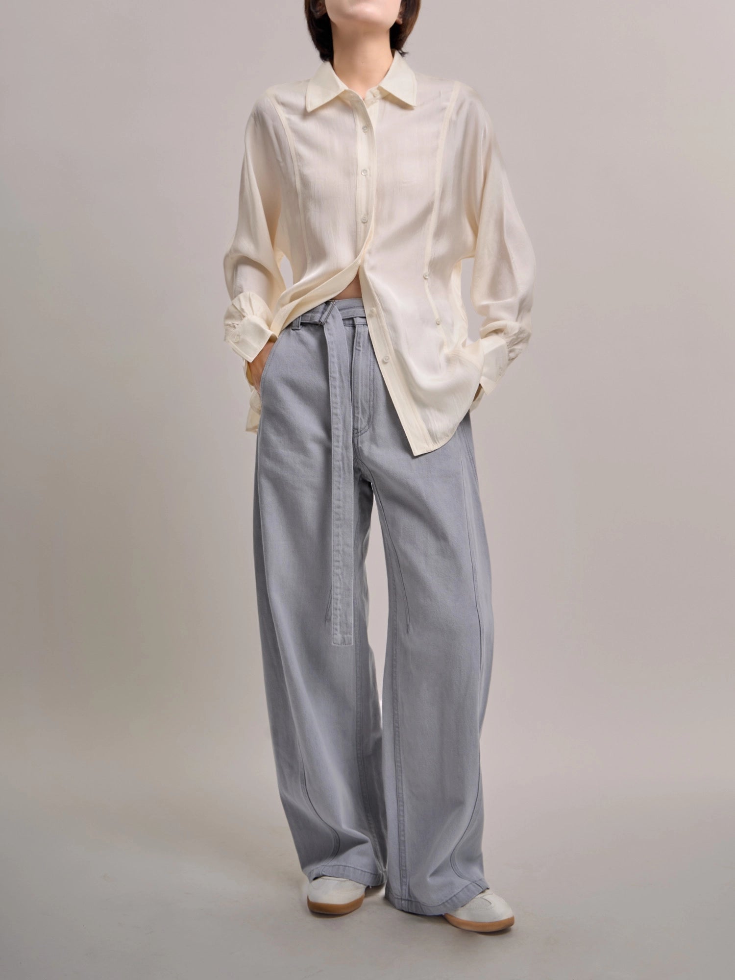 Model wearing light blue Curved Cocoon Jeans with curved seams, full-body studio shot styled with cream shirt.