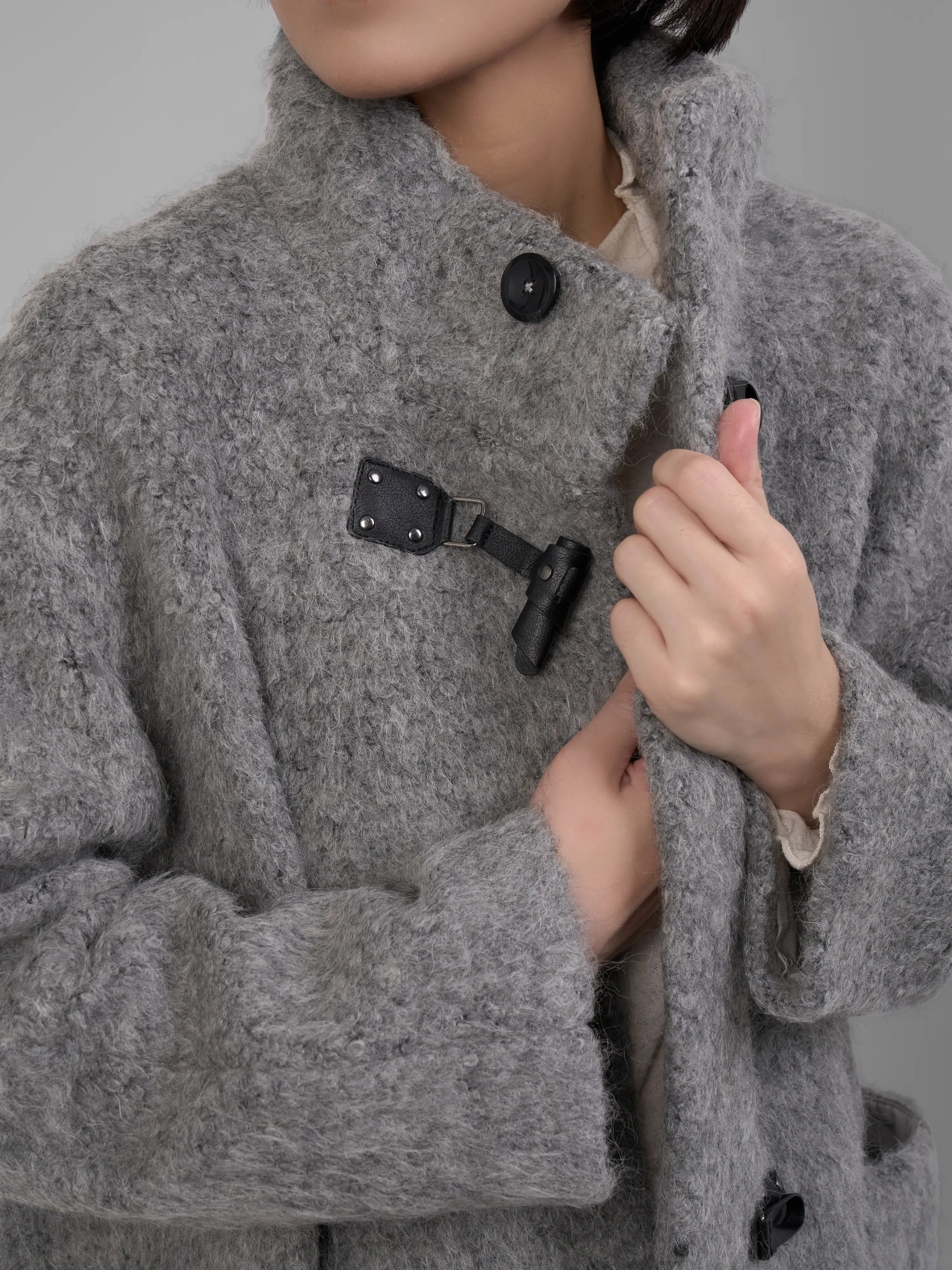 Close-up detail of the Grey Wool Toggle Coat showing the textured wool fabric and leather toggle fastening.