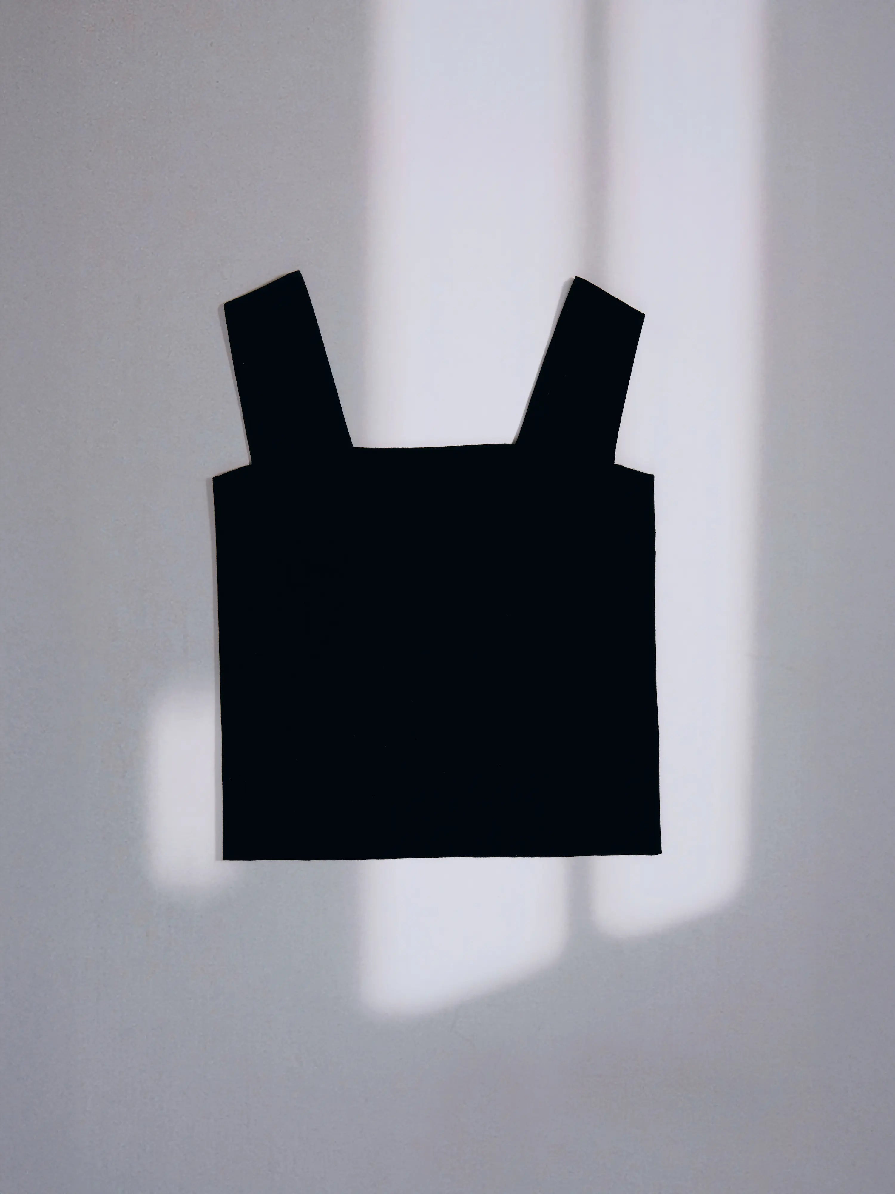 Black Minimal Square Neck Shell hanging against a wall with natural light and shadow.