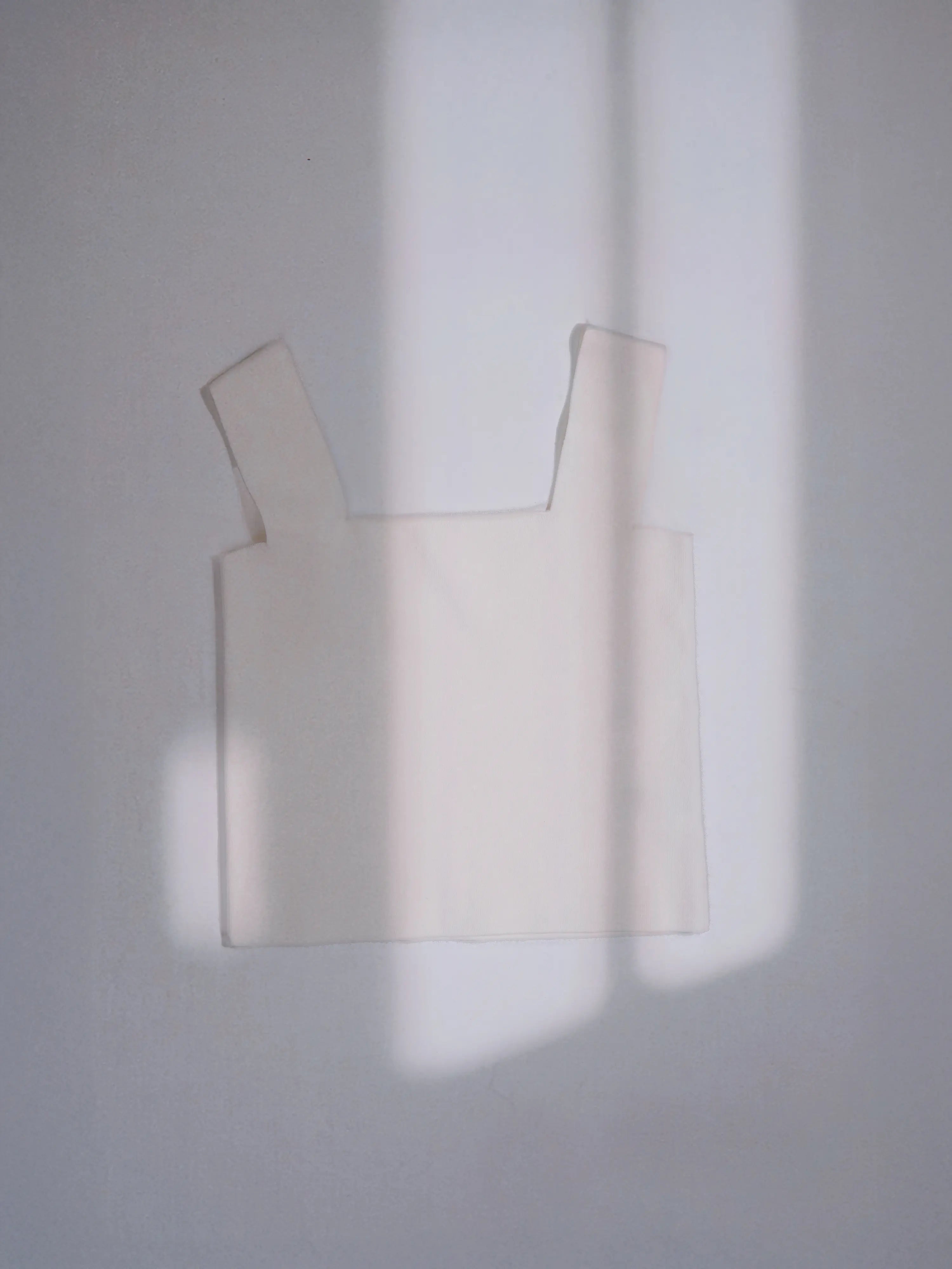 Ivory Minimal Square Neck Shell hanging against a wall with soft natural light.