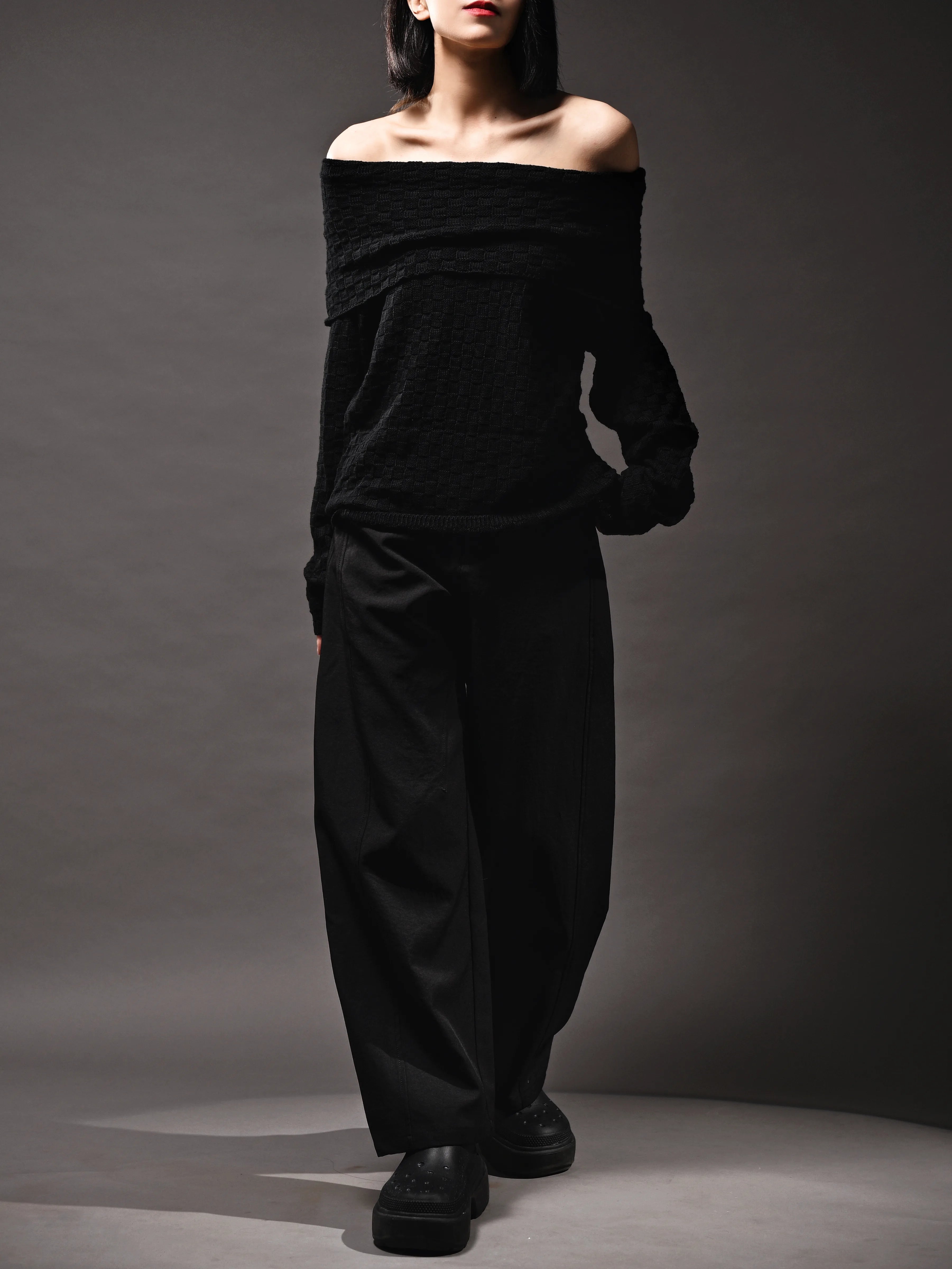Model walking in black off-shoulder top, soft knit texture, elegant draped silhouette.