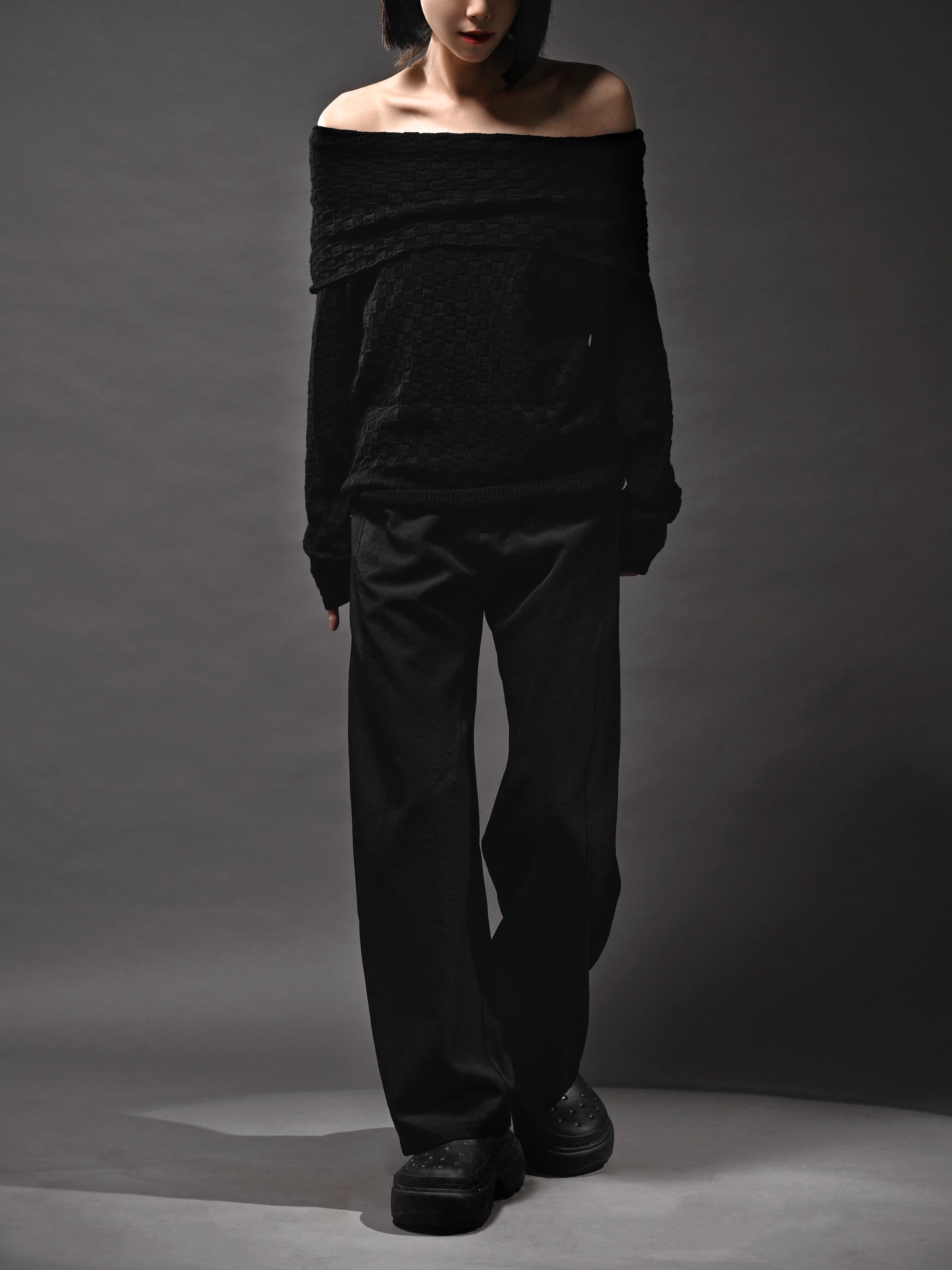 Black off-shoulder knit top on model, full-body front view, textured fabric, wide neckline styling.