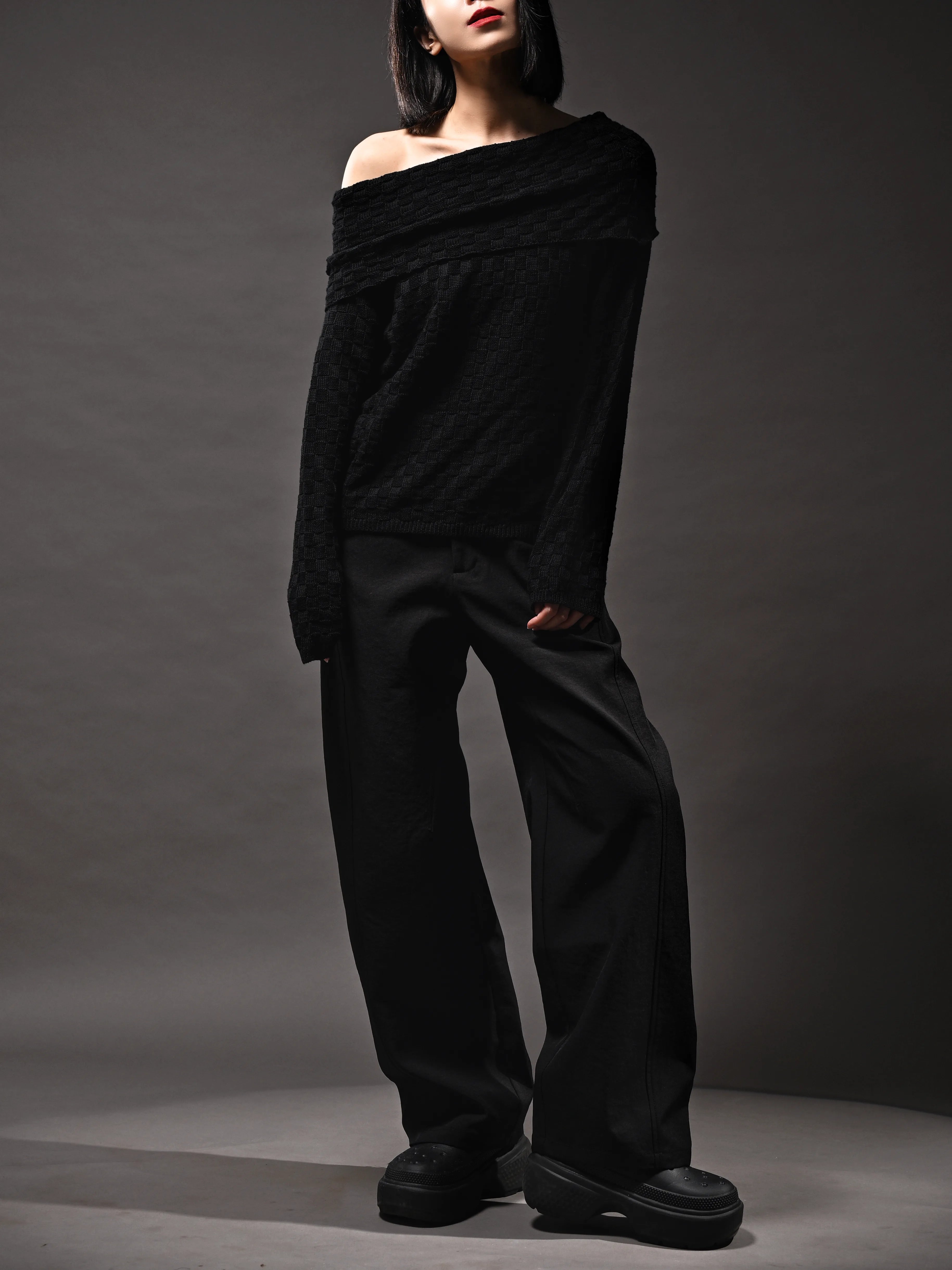 Side angle of black off-shoulder knit top, slouch fit, paired with black trousers for minimal styling.