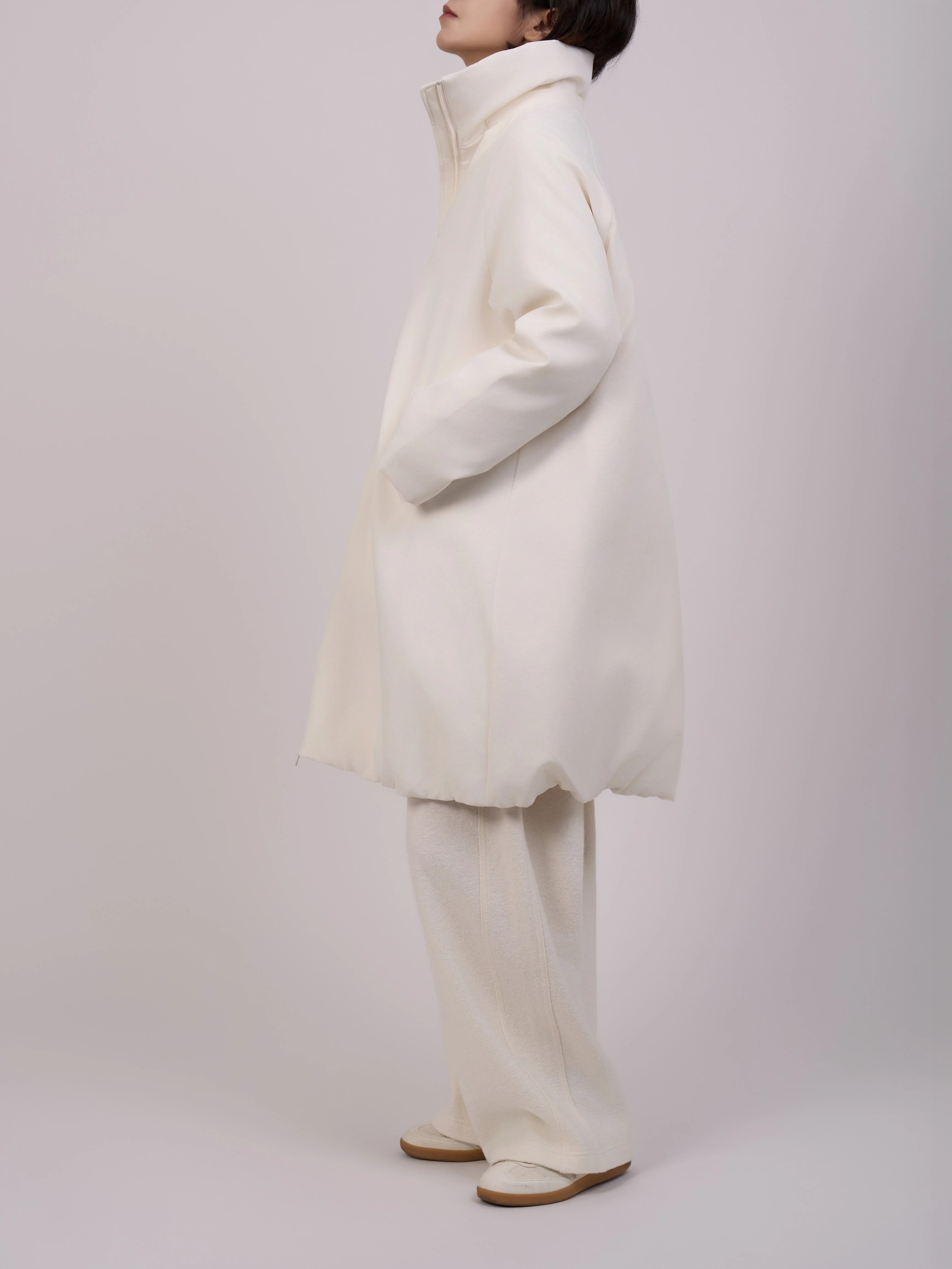 The model stands sideways to showcase the garment's profile.