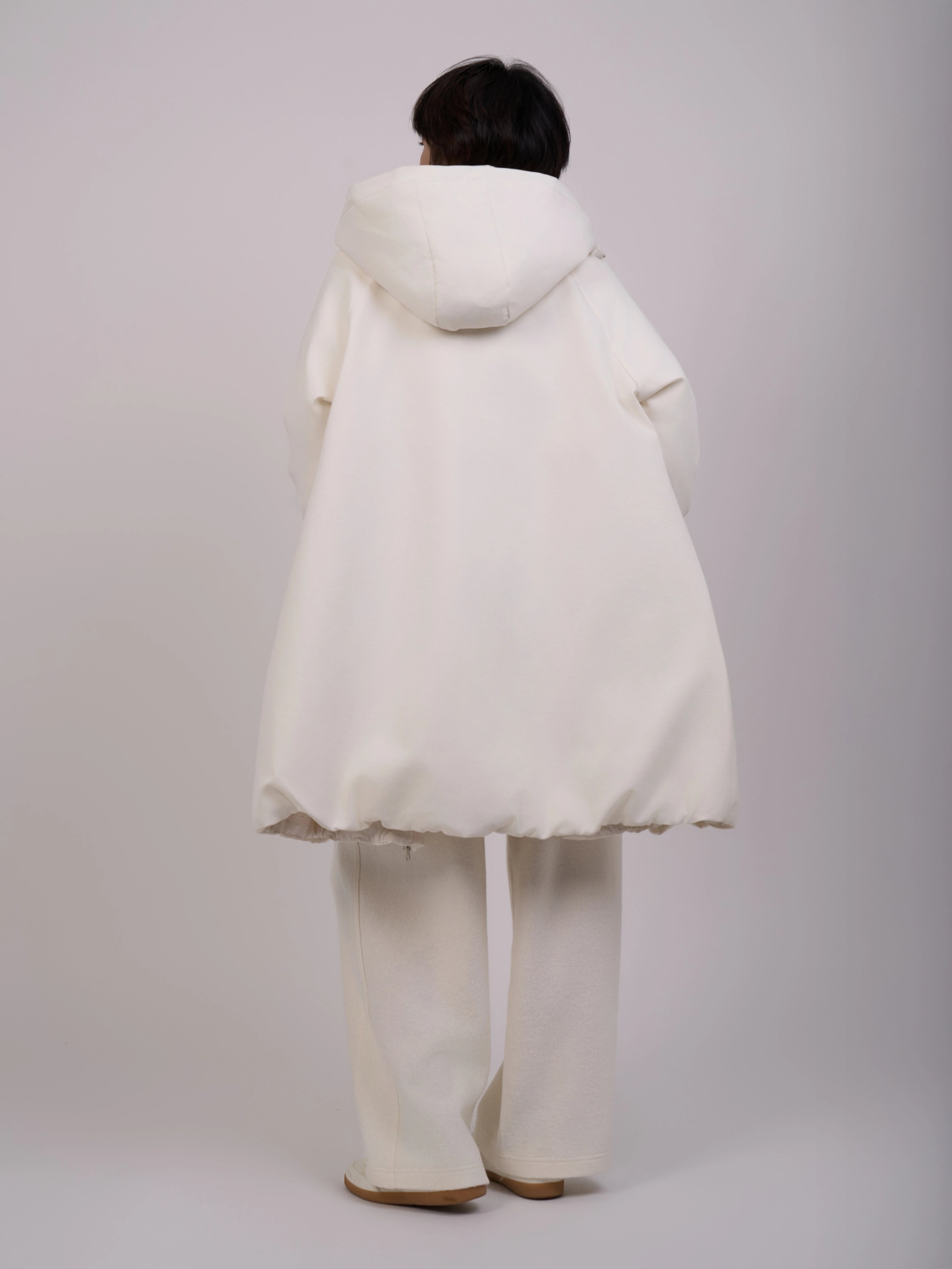 The model stands with her back to the camera, showcasing the back details of the garment.