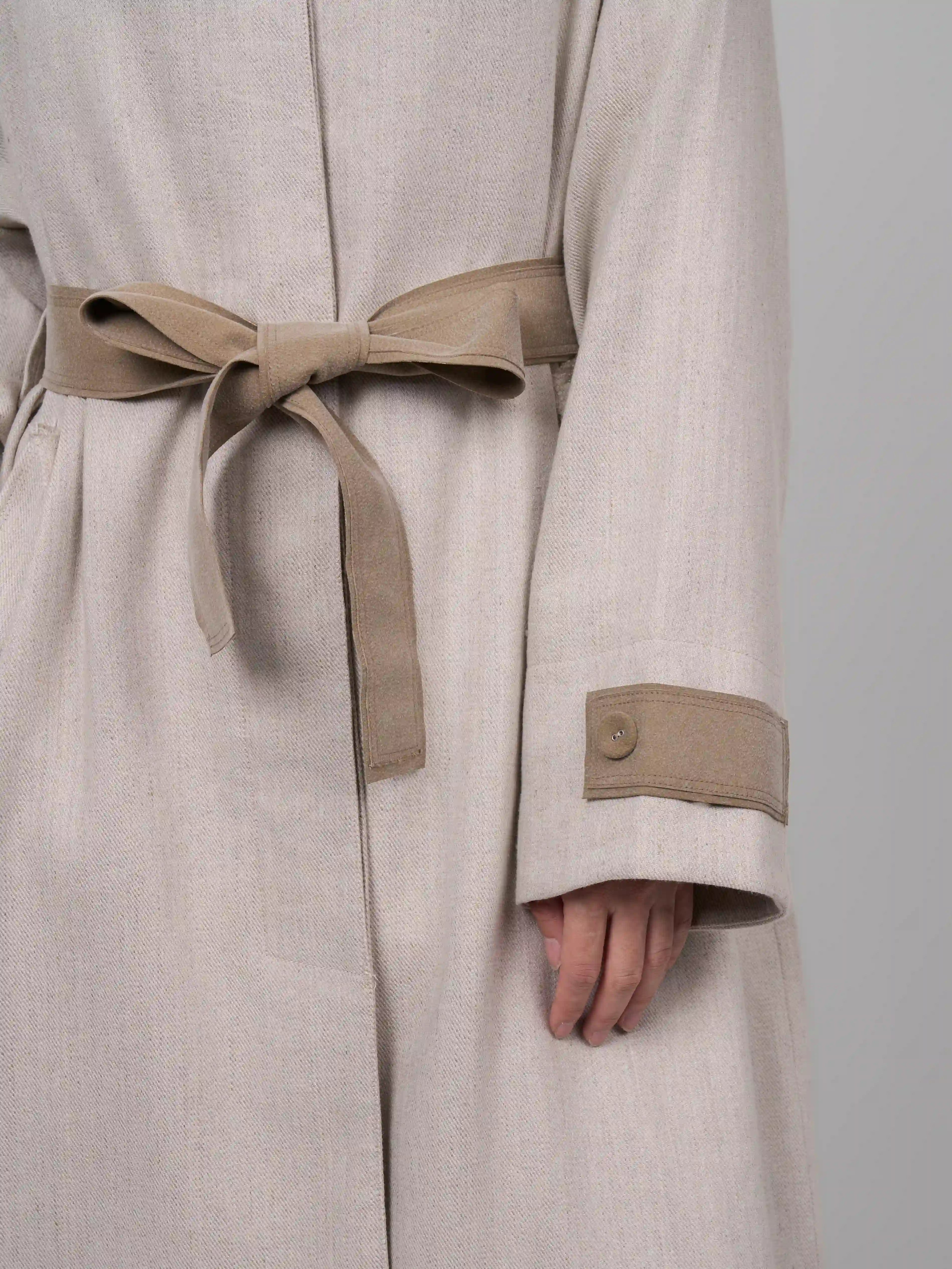 Close up sleeve cuff detail of beige rain dew linen wool coat showing natural texture and contrast trim