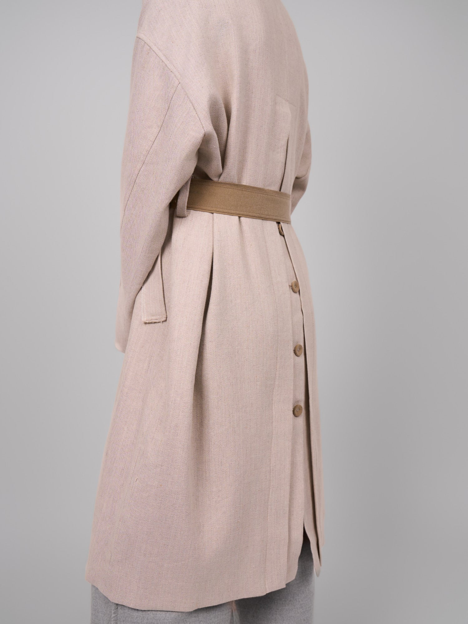 Three-quarter back view of beige Rain Dew linen–wool coat, belted waist and buttoned back detail.