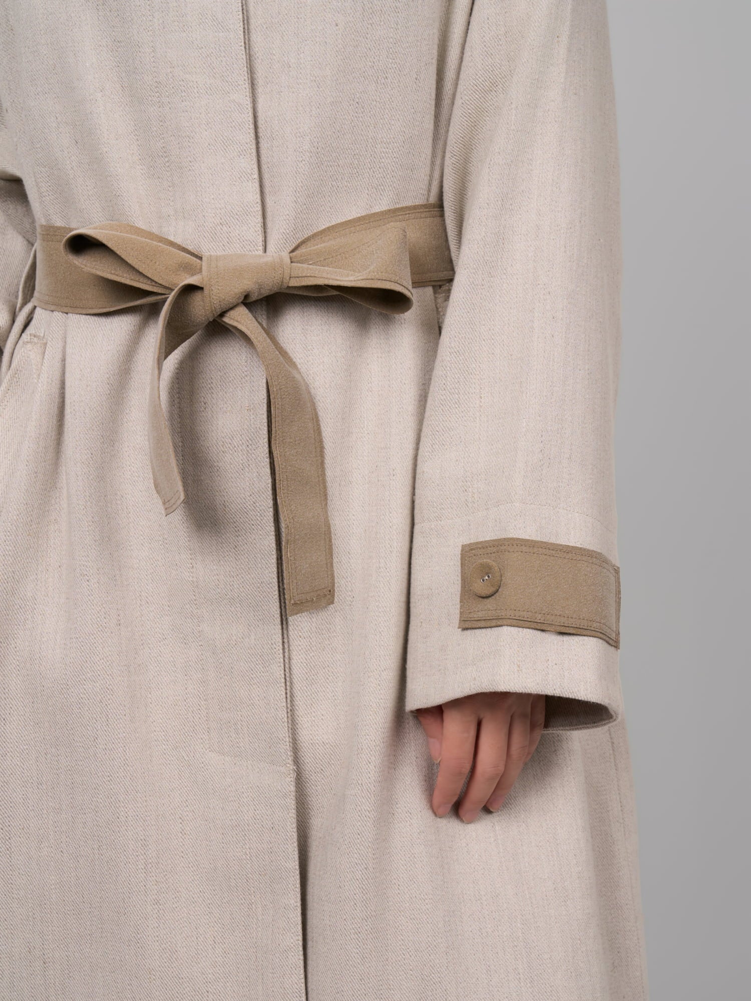 Close-up of waist belt and cuff detail on beige Rain Dew linen–wool coat, highlighting contrast trim.