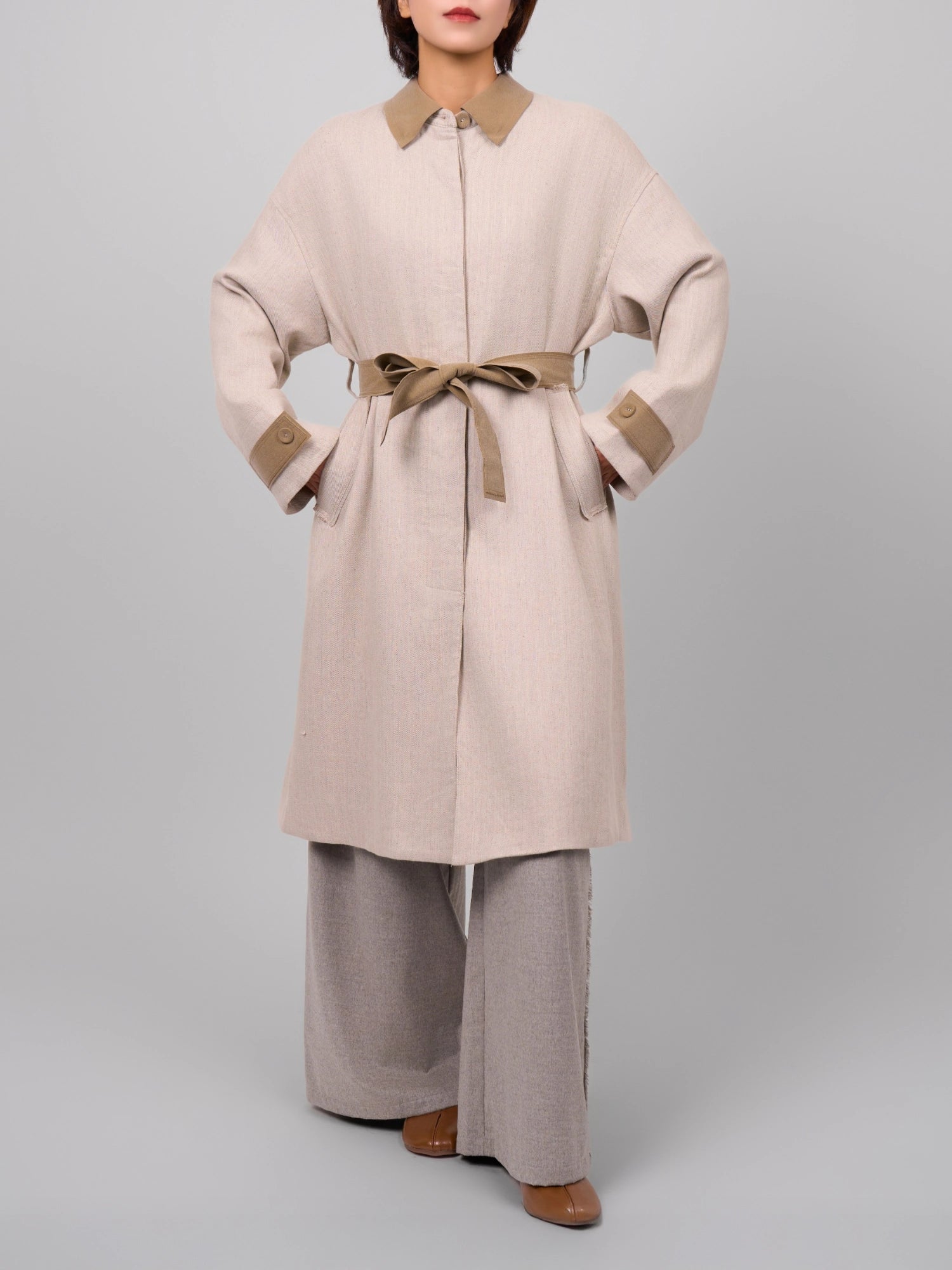 Beige Rain Dew linen–wool coat with belt cinched, cocoon silhouette and contrast cuffs in studio light.