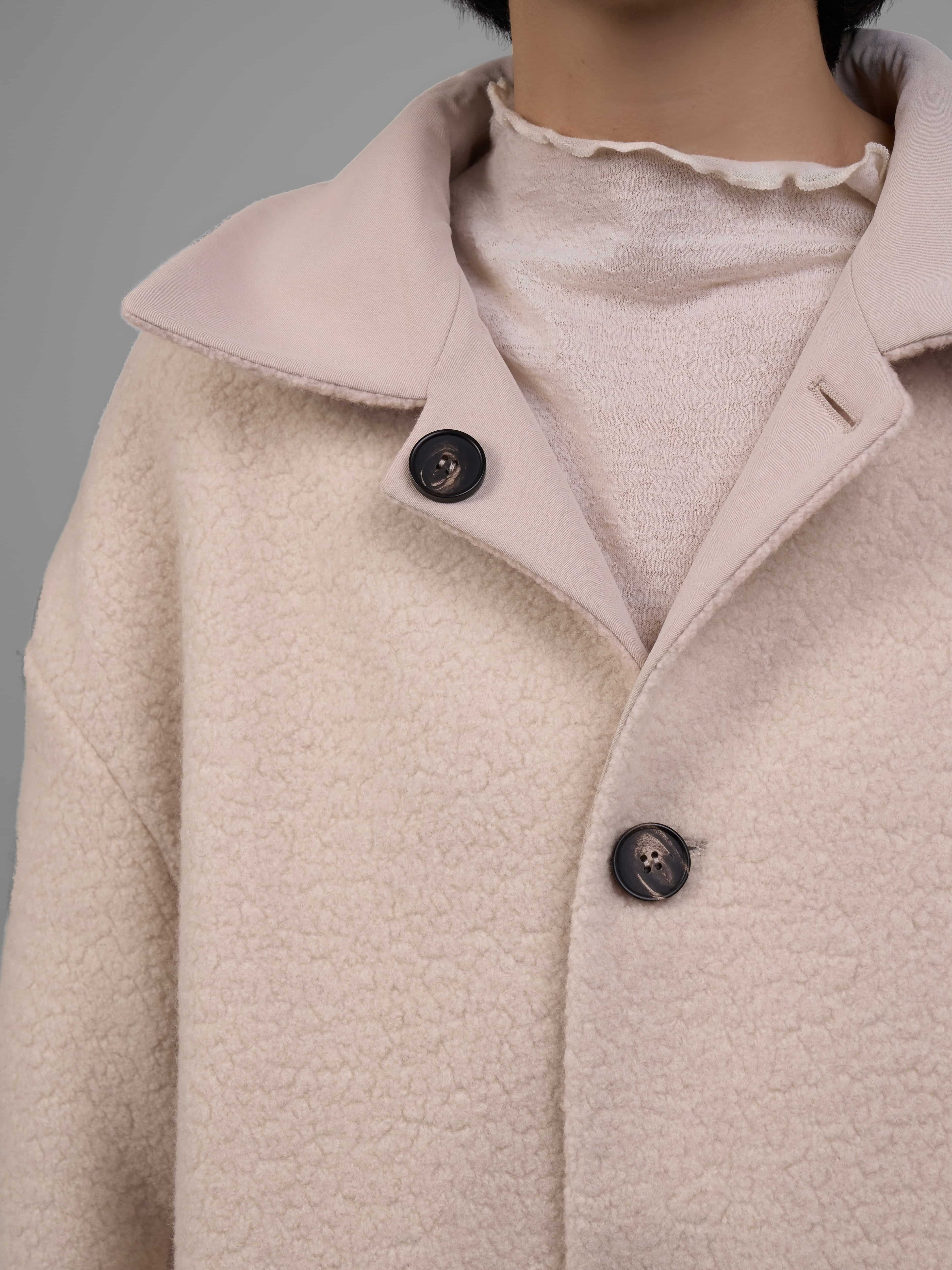 Close-up view of button placket on reversible wool coat, highlighting craftsmanship and texture.